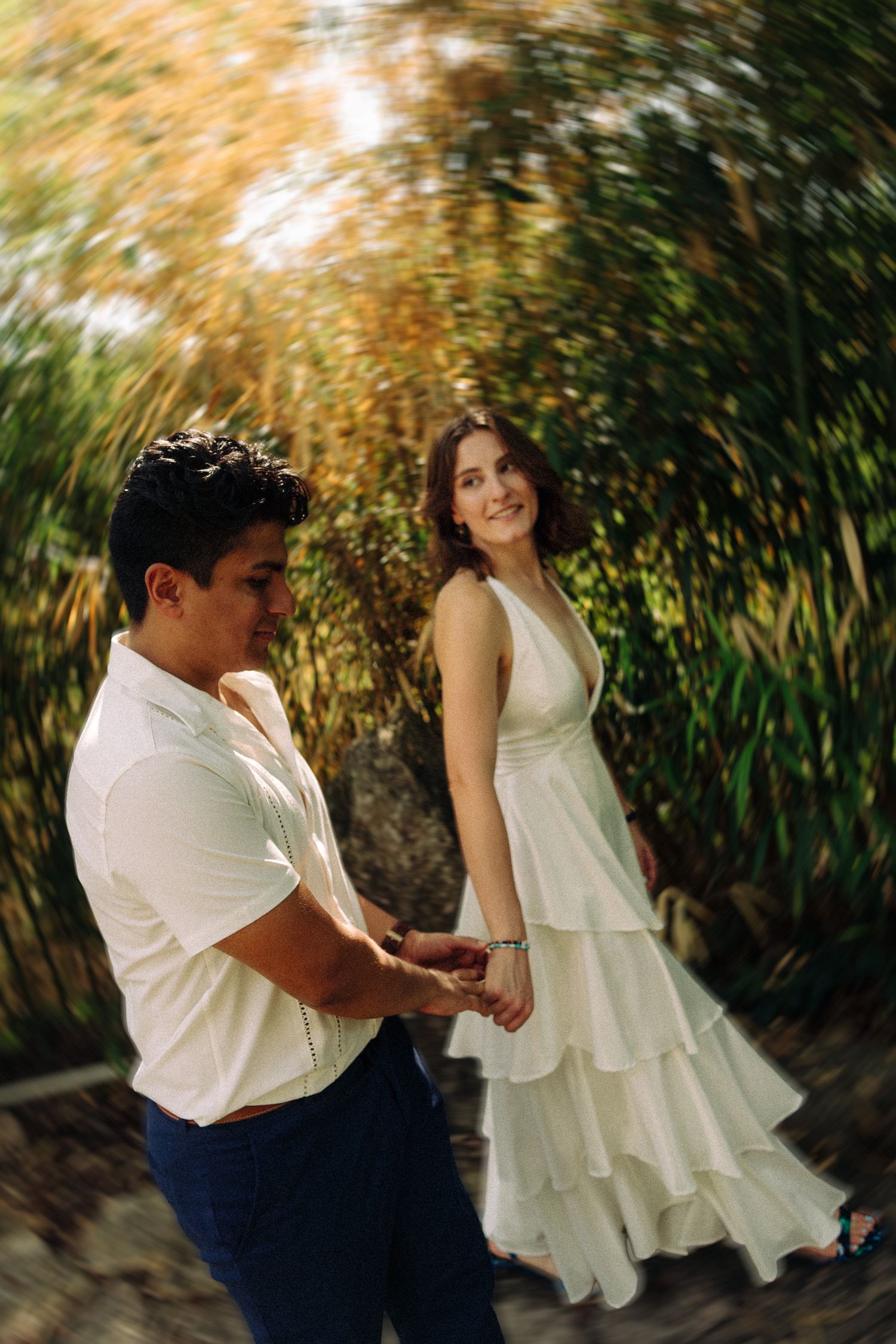 Couple in coordinated white and navy outfits dancing in a garden with motion blur effect.