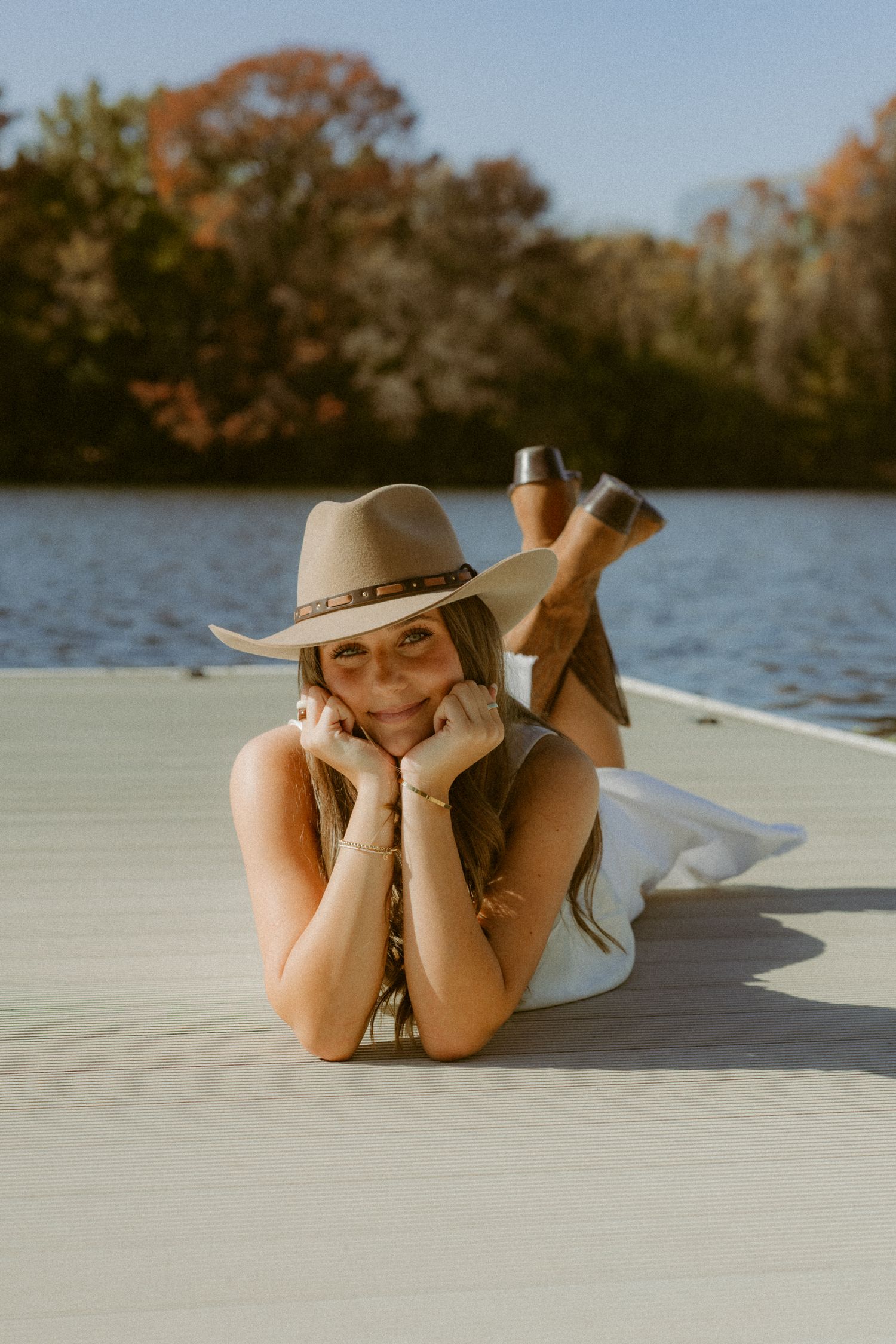 A relaxed pose on a dock wearing a wide-brimmed hat during a sunny autumn day by the lake.