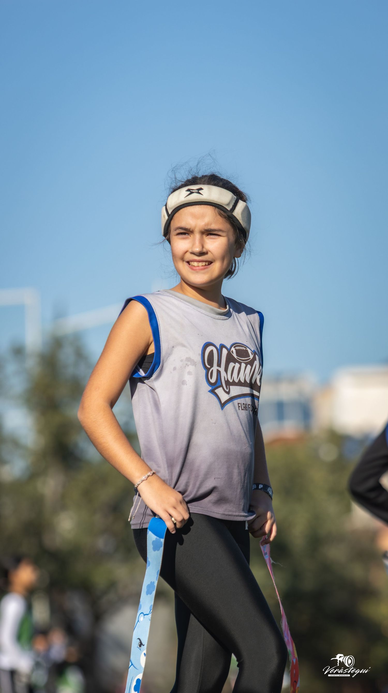 Softball player in gray and blue uniform smiling during practice outdoors on sunny day.