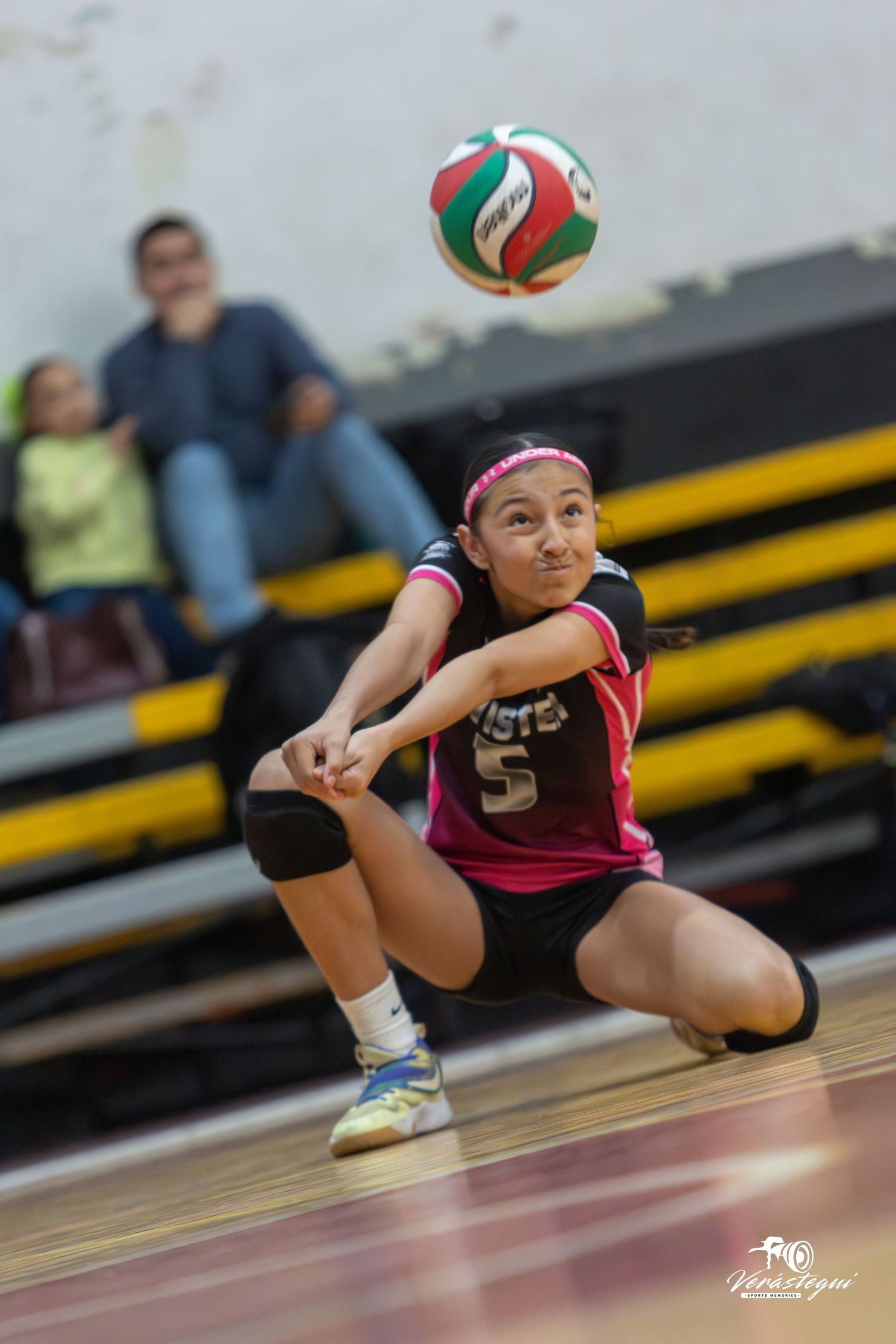 A volleyball player in a maroon uniform dives to save a ball during an intense match on the court.