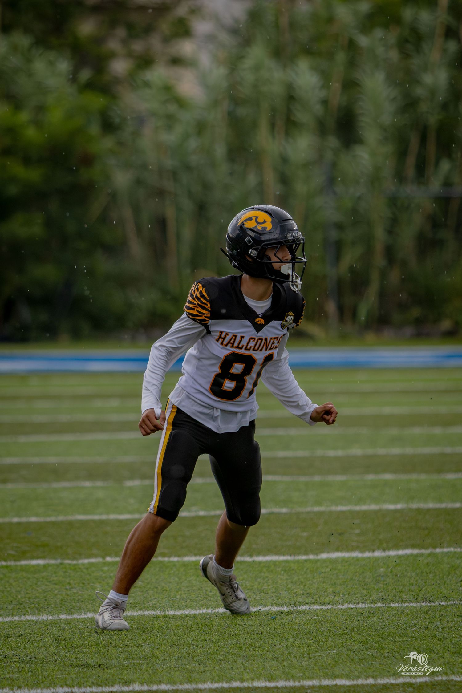Football player wearing Falcons jersey number 81 running on turf field during rainy game day.