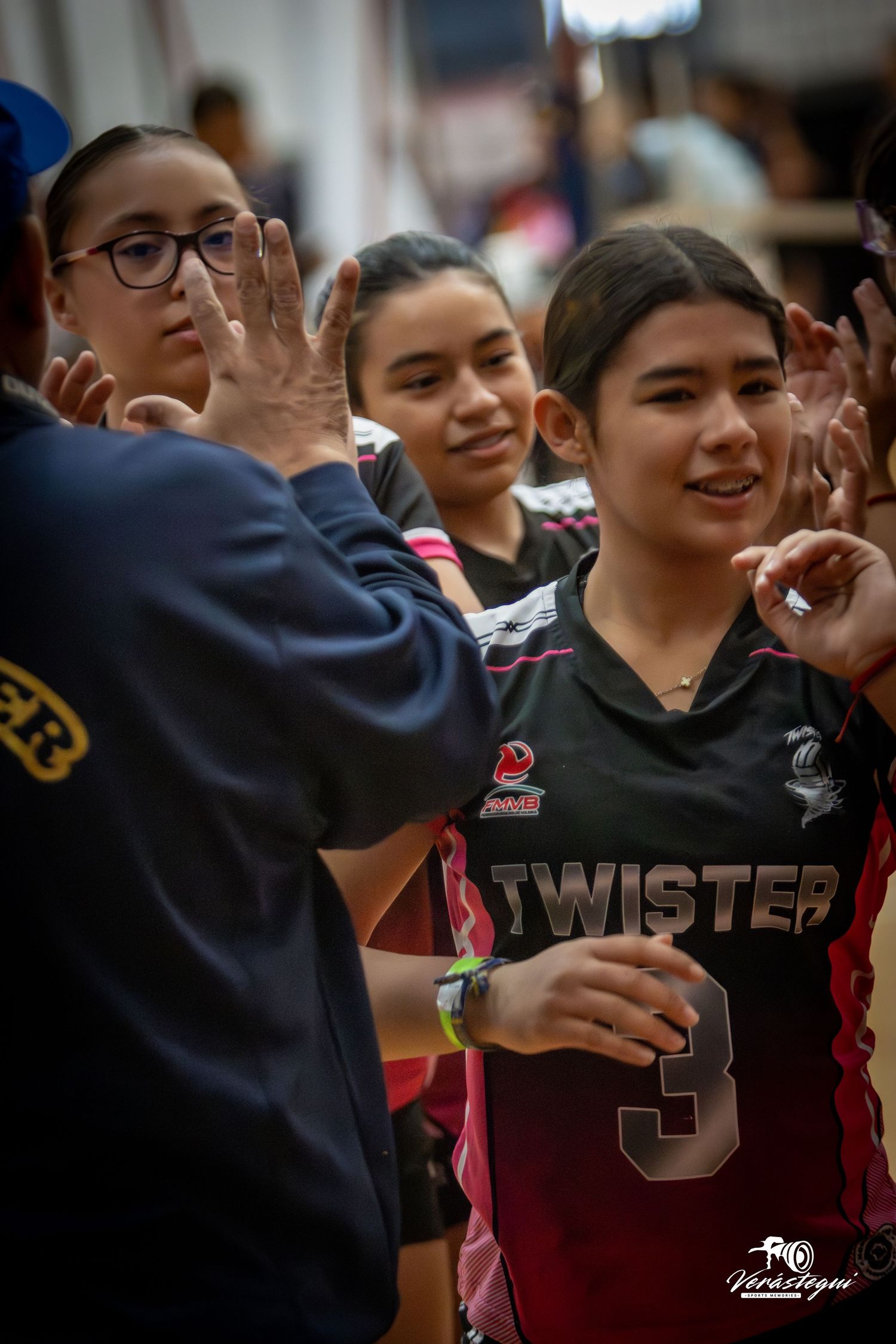 A group of students in sports uniforms gather together smiling and celebrating in a gymnasium.