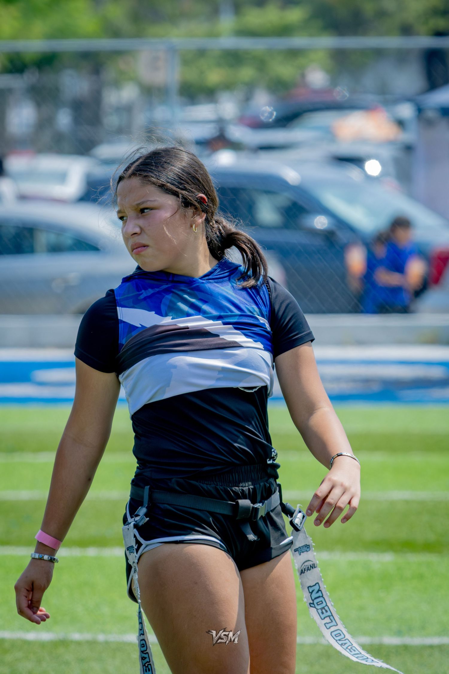 Young female athlete in blue and black uniform walks on green field during outdoor sports competition.