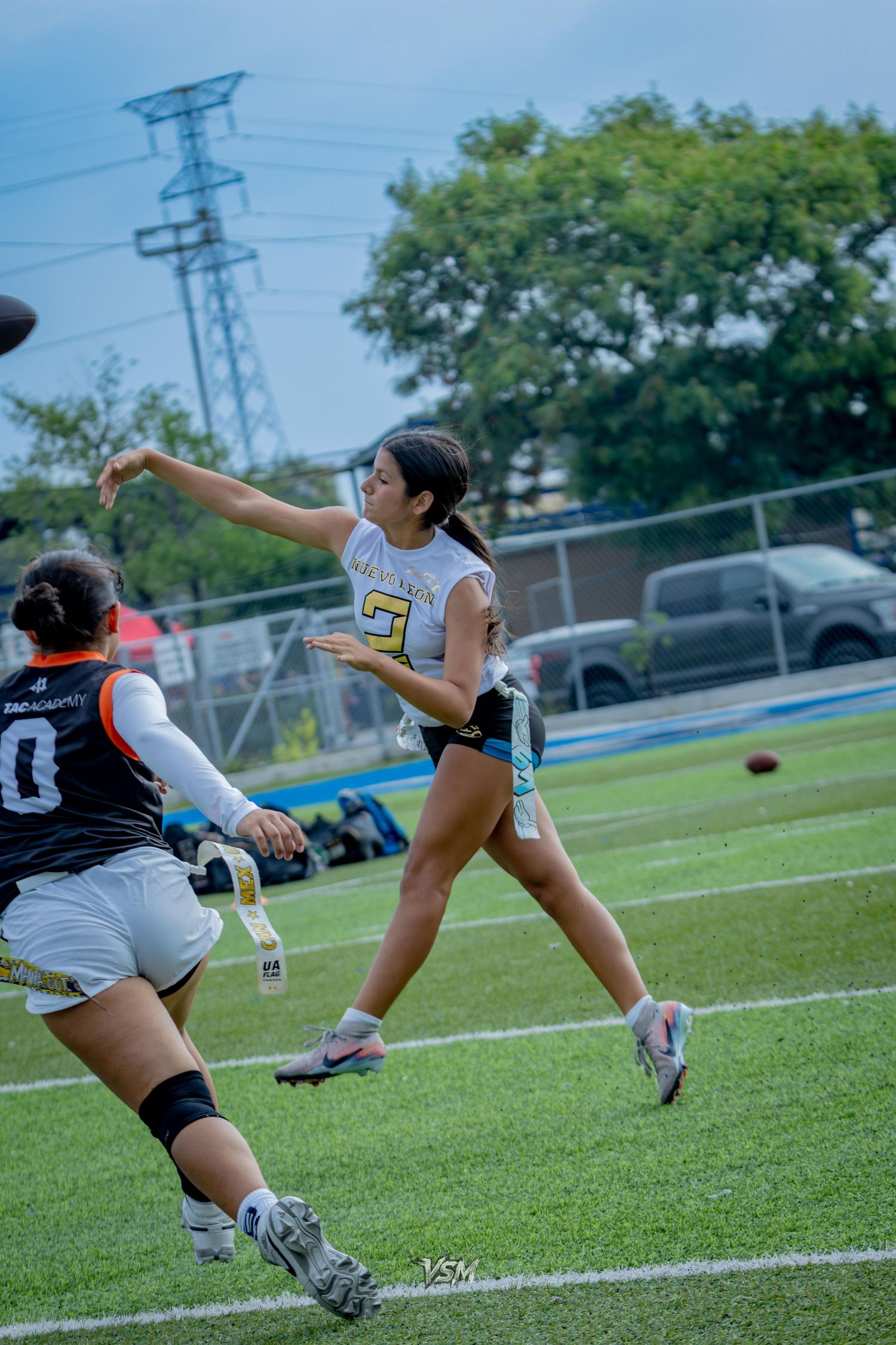 Female flag football player throws a pass during a game on a turf field while a defender rushes in.