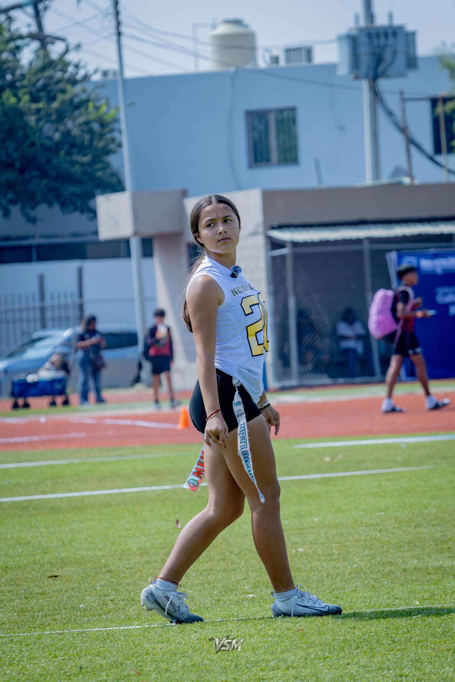 Female flag football player in white jersey walking on green turf field during a game.