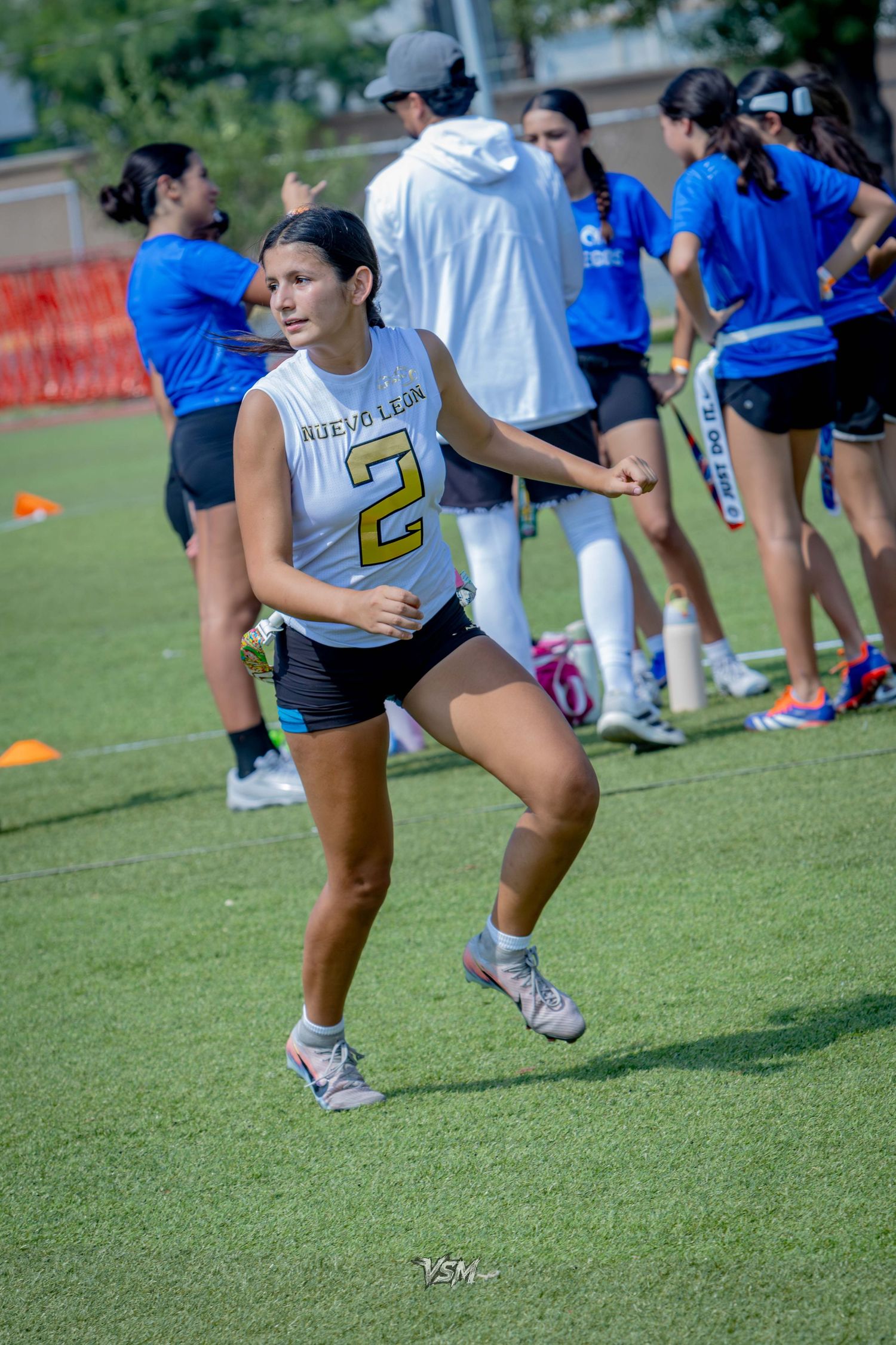 Female athlete wearing jersey number 2 runs on a green turf field during an outdoor sports event.