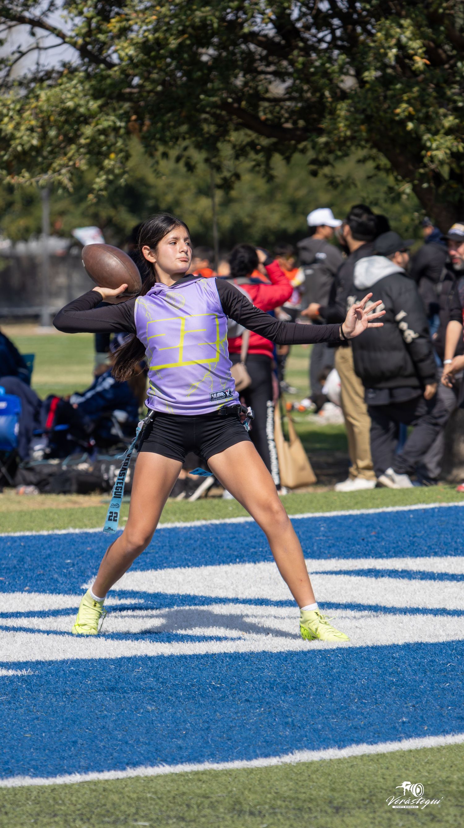 Track and field athlete in purple jersey prepares to throw shot put at outdoor competition on blue surface.