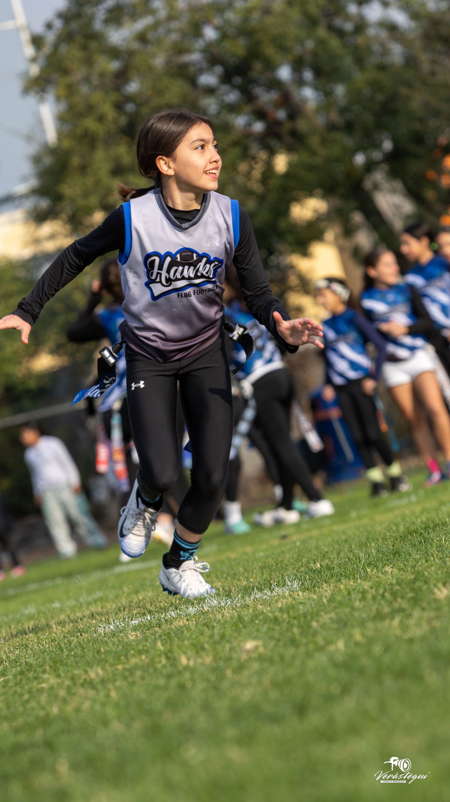 Young cheerleader in blue and white uniform performs athletic move on grass field during outdoor practice session.