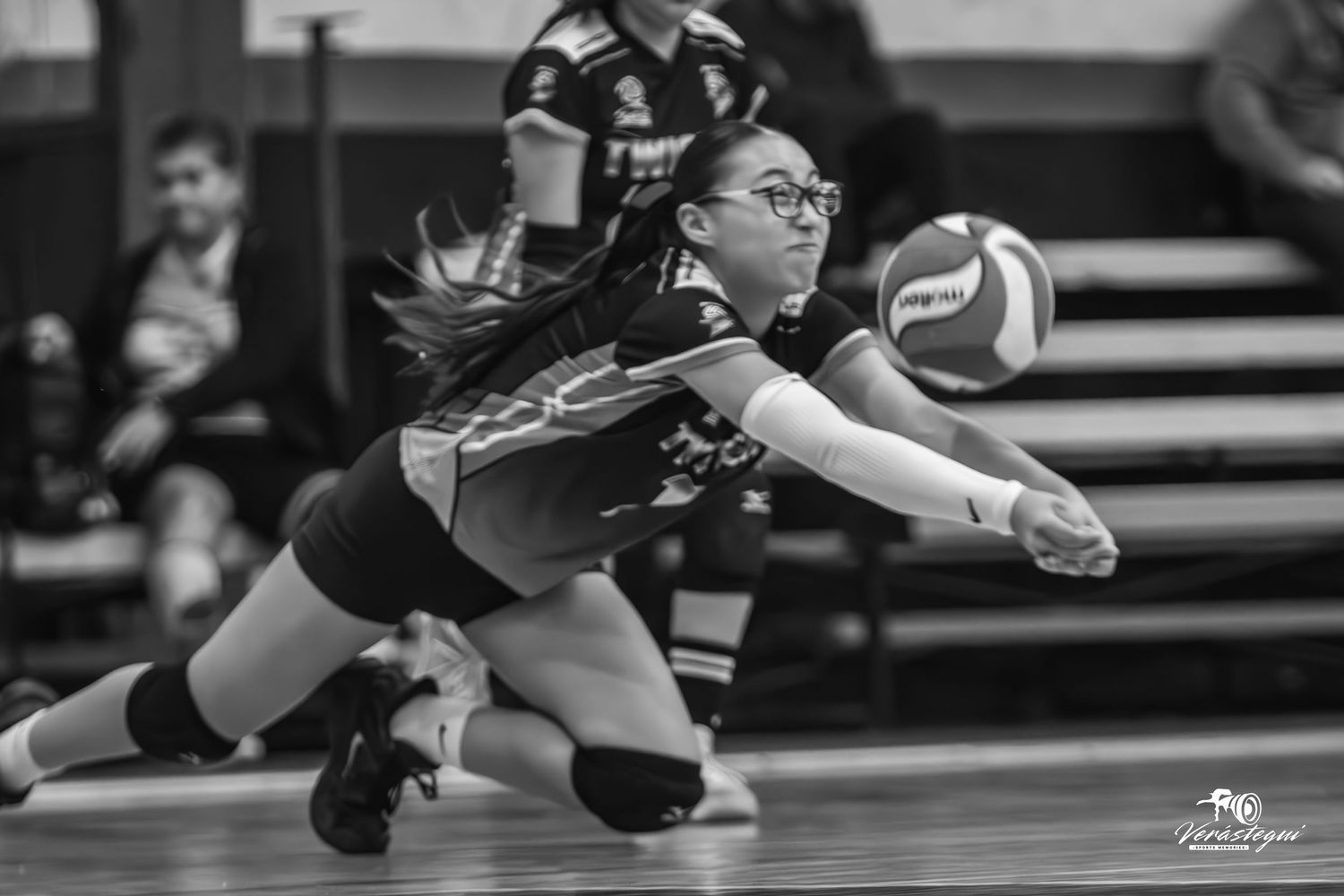 A sequence of black and white photos showing a volleyball player diving and stretching to save the ball during a match.