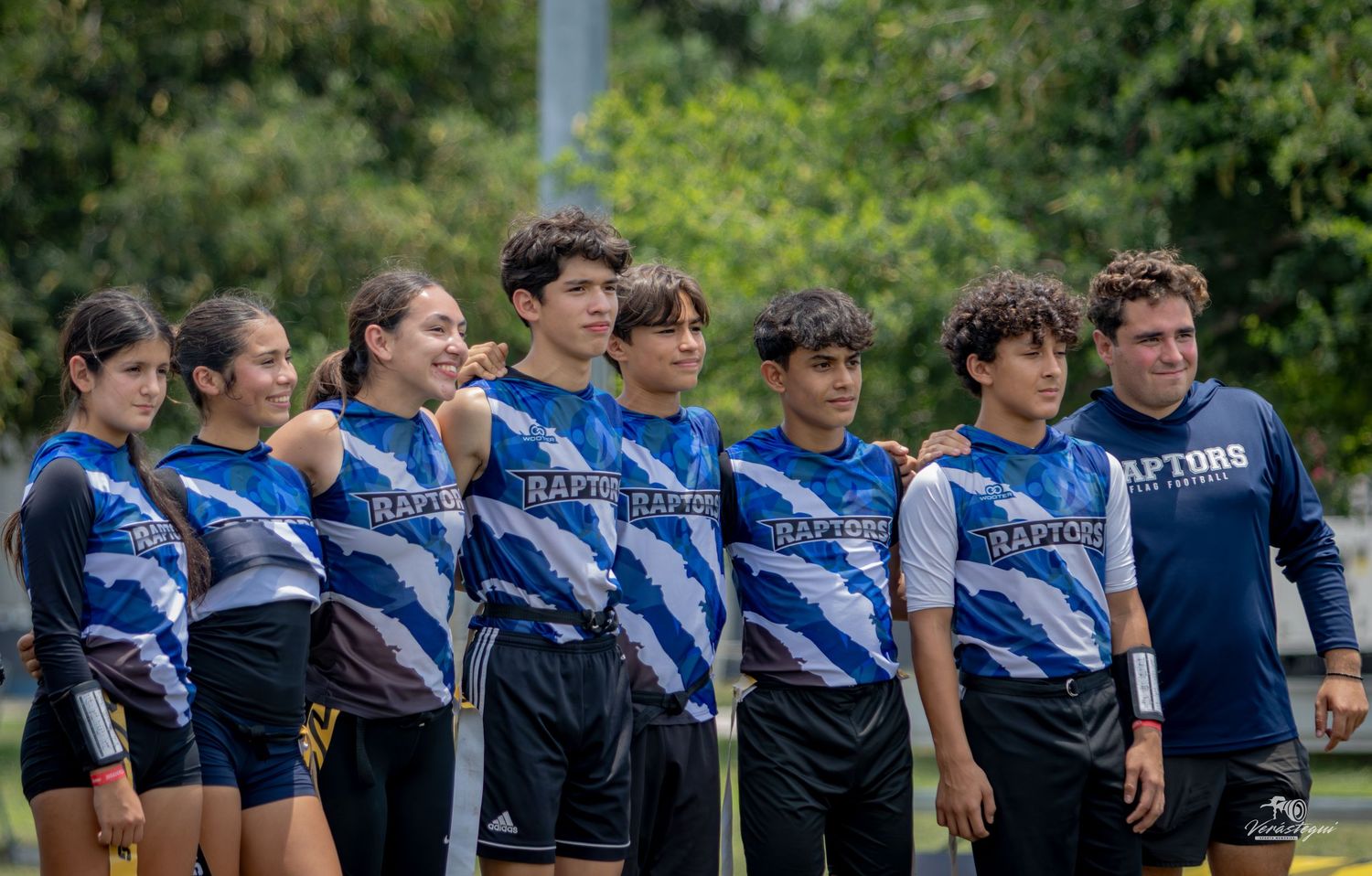 Youth Raptors sports team members in blue jerseys posing together outdoors during a team event.