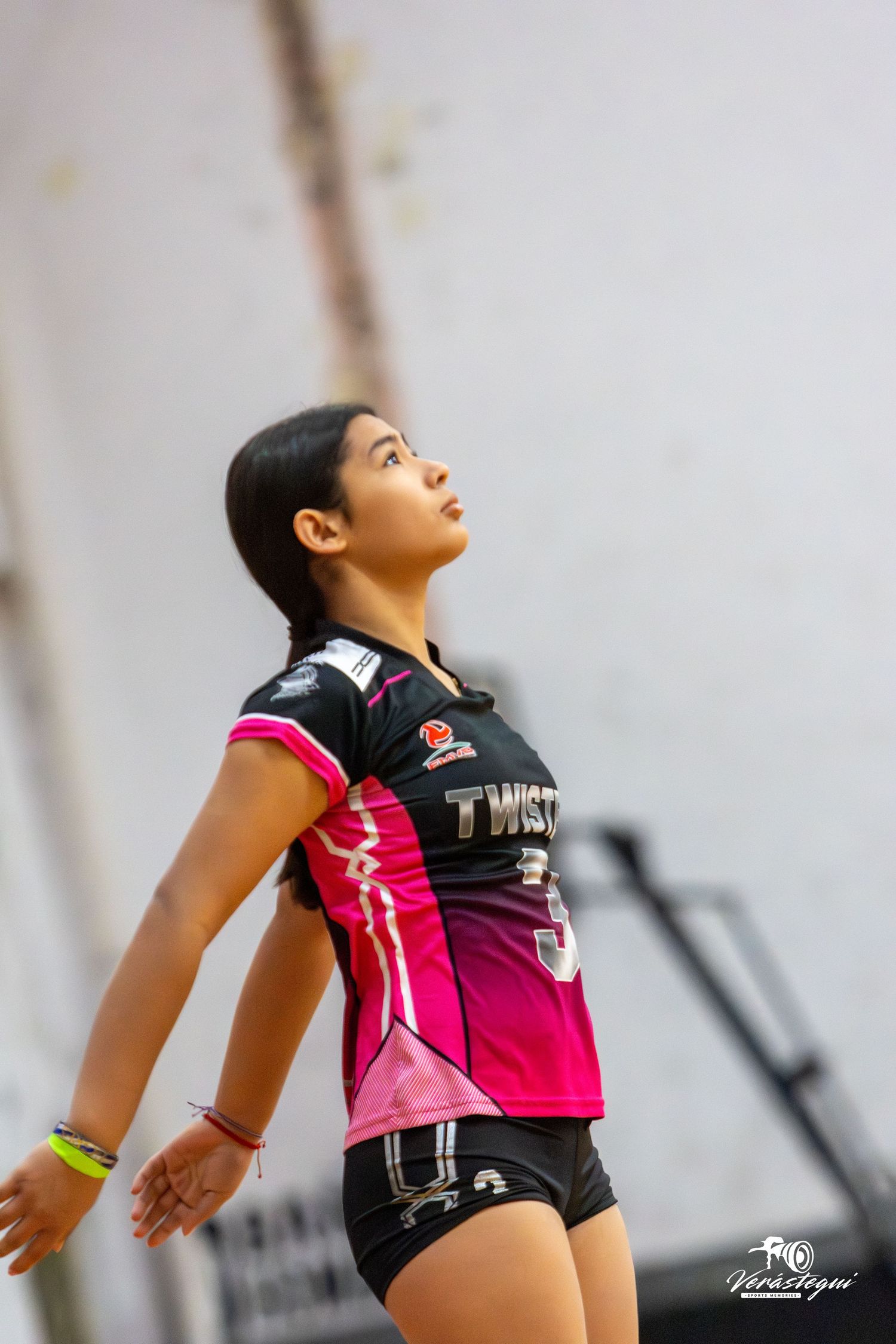 Volleyball player in black and pink uniform leaps upward during a match, demonstrating dynamic athletic movement.