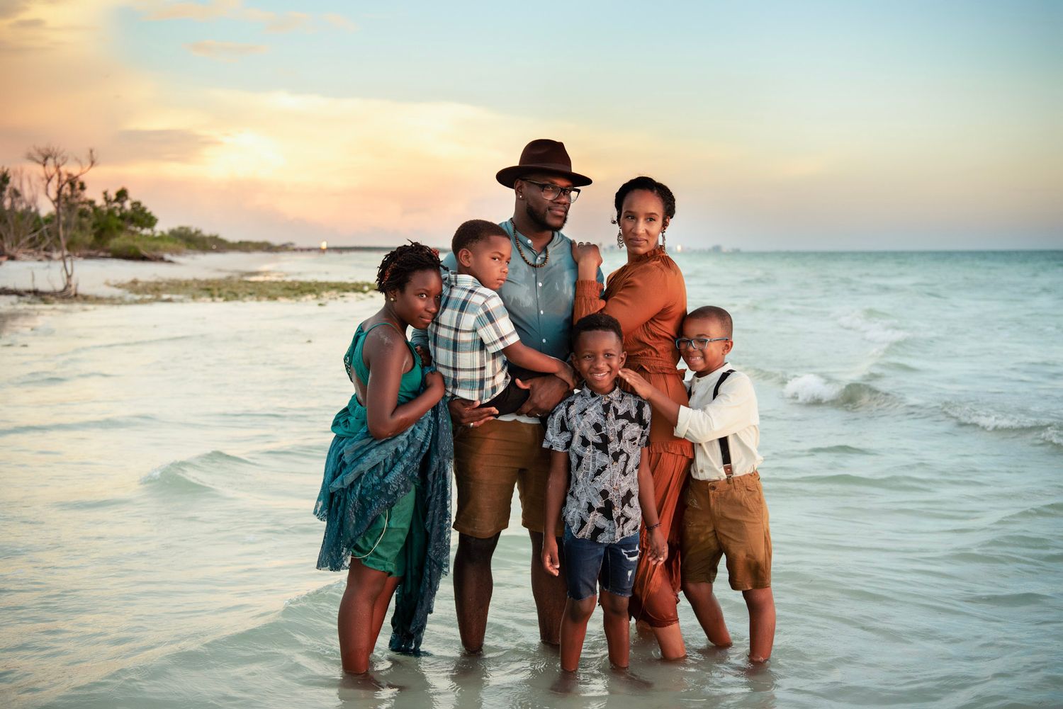 Family of five standing in the Gulf waters during a sunset beach portrait session on Florida's coast while they're on vacation in Dunedin.