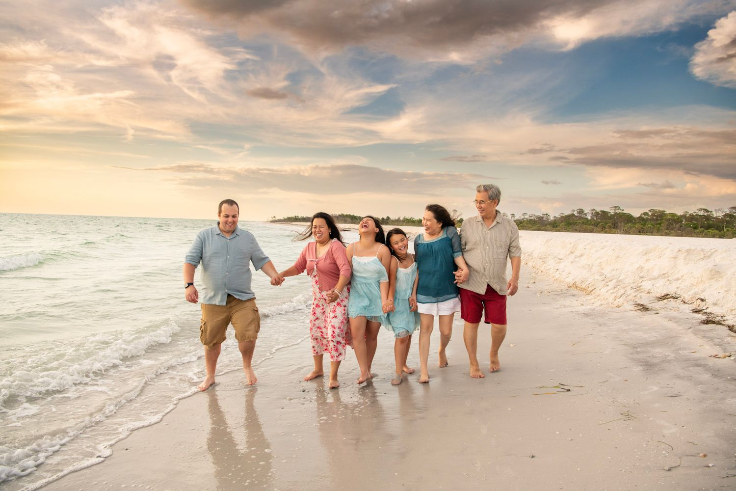 Happy extended family walking happily barefoot along the shoreline during a sunset beach photography session in Florida.