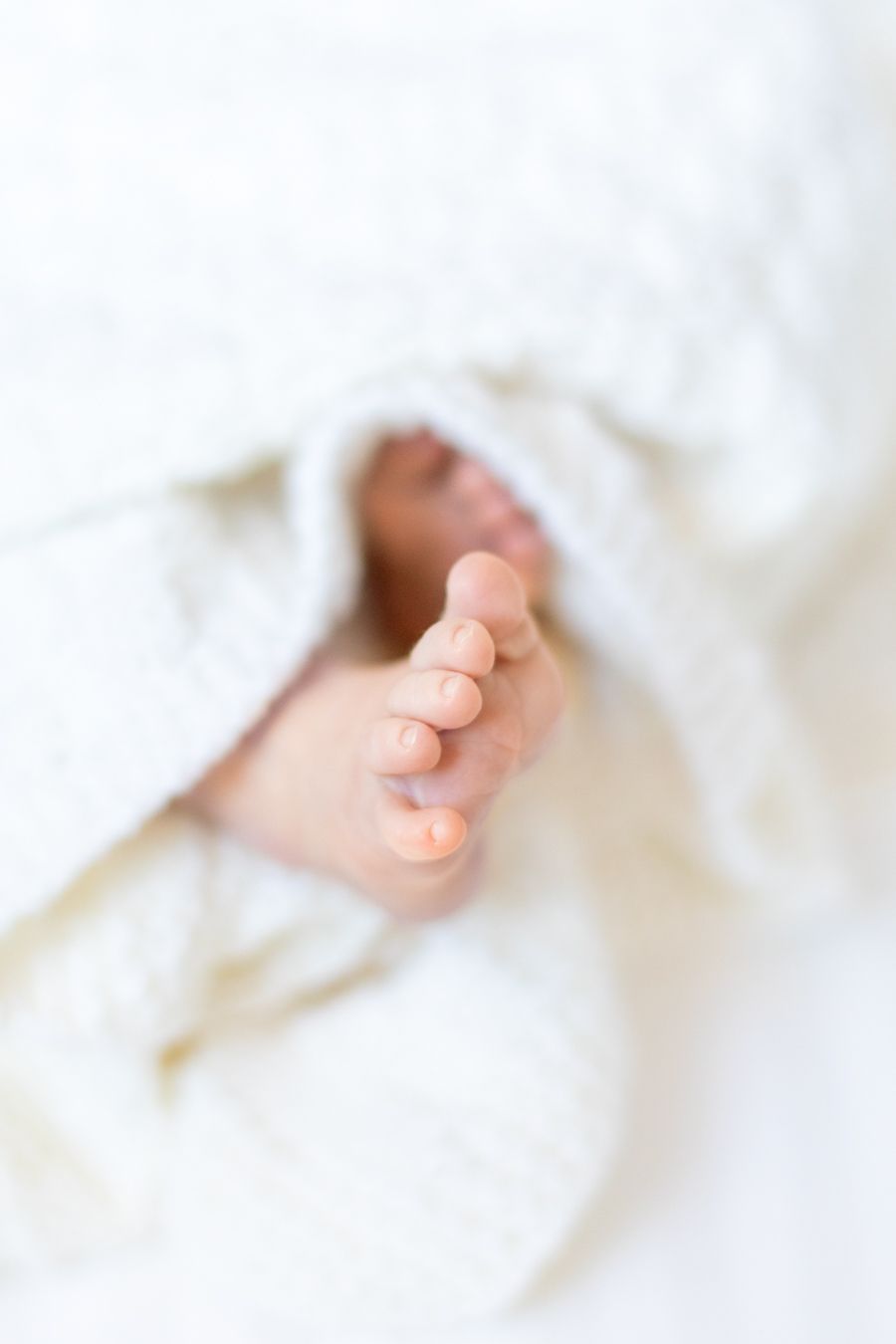 Vauvan varpaat pilkistävät valkoisen peiton alta newborn-kuvauksessa Nummelassa.