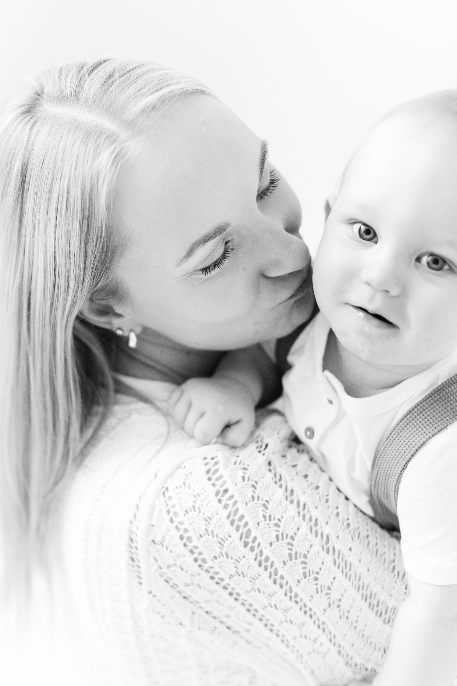 Äiti suukottaa lastaan yksivuotiskuvauksessa studiossa Vantaalla.