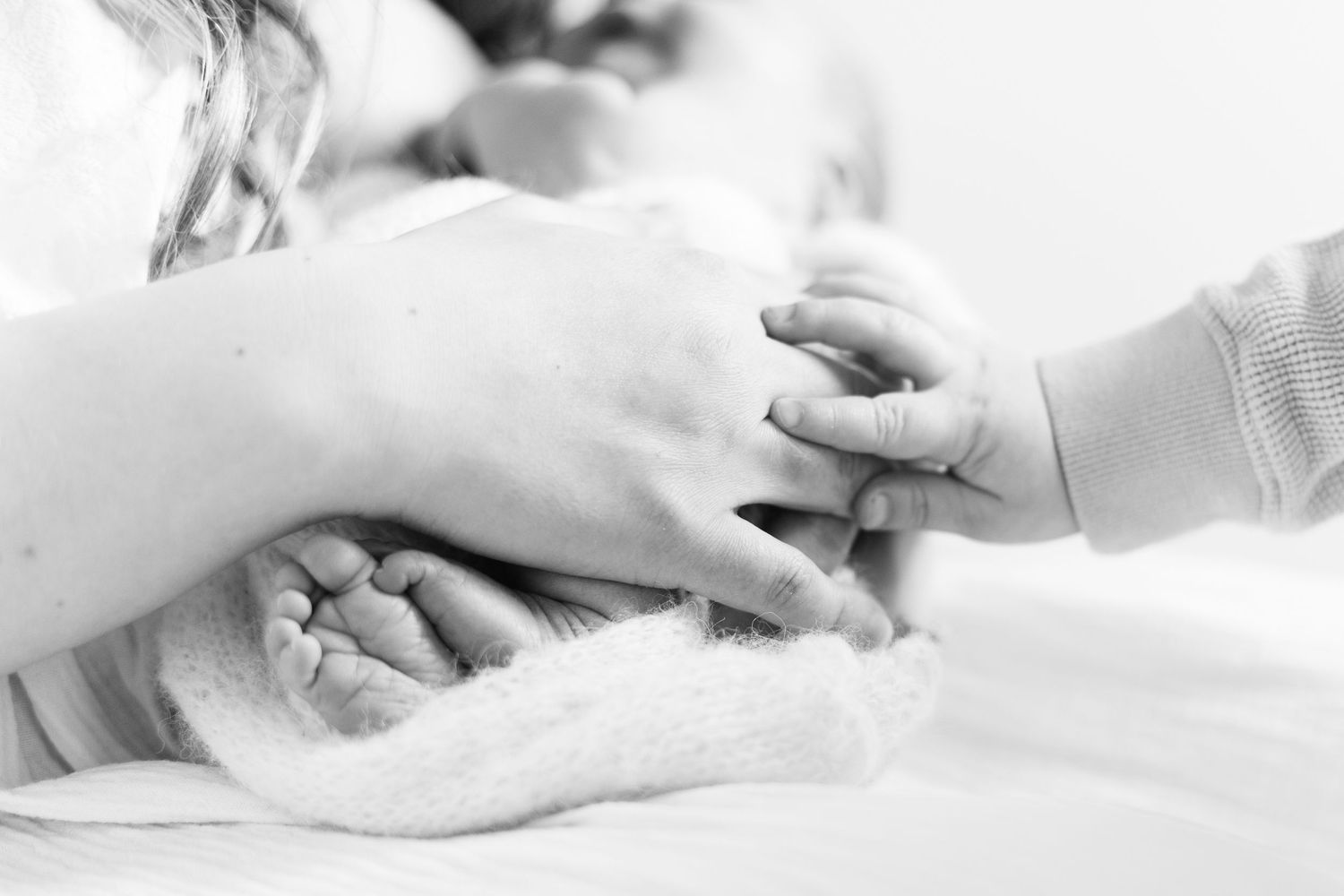 Koko perheen kädet vastasyntyneen vauvan ympärillä newborn-studiokuvauksessa Vantaalla.