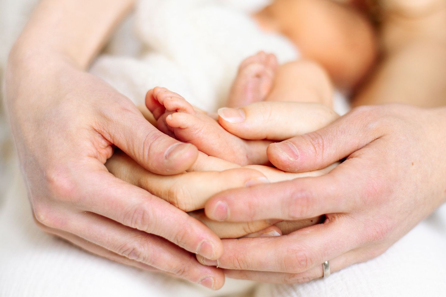 Vastasyntyneen vauvan pikkuiset jalat vanhempiensa käsissä newborn-studiokuvauksessa Vantaalla.