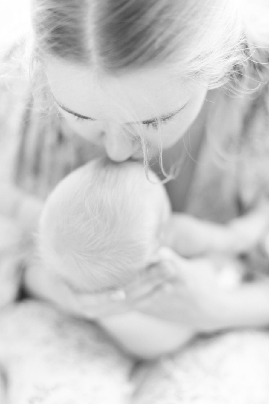 Mustavalkokuva äidistä suukottamasta vastasyntynyttä pienokaistaan. Newborn-kotikuvaus Lohjalla ja Espoossa.