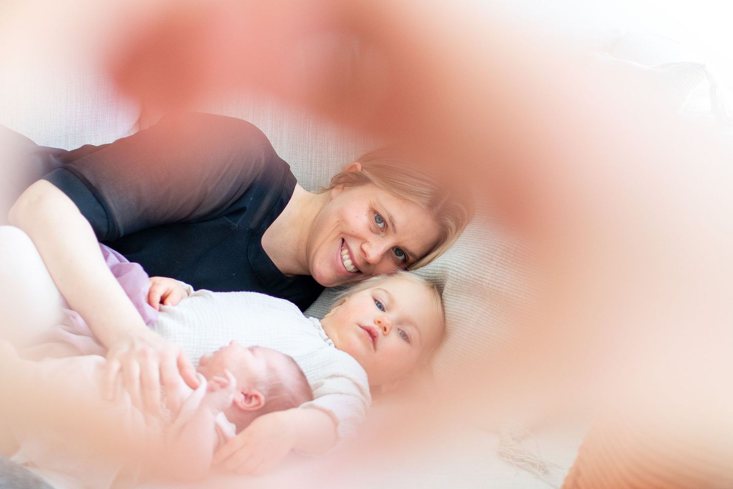 Isä kurkkaa äitiä ja vastasyntynyttä vauvakuvauksessa Lohjalla.