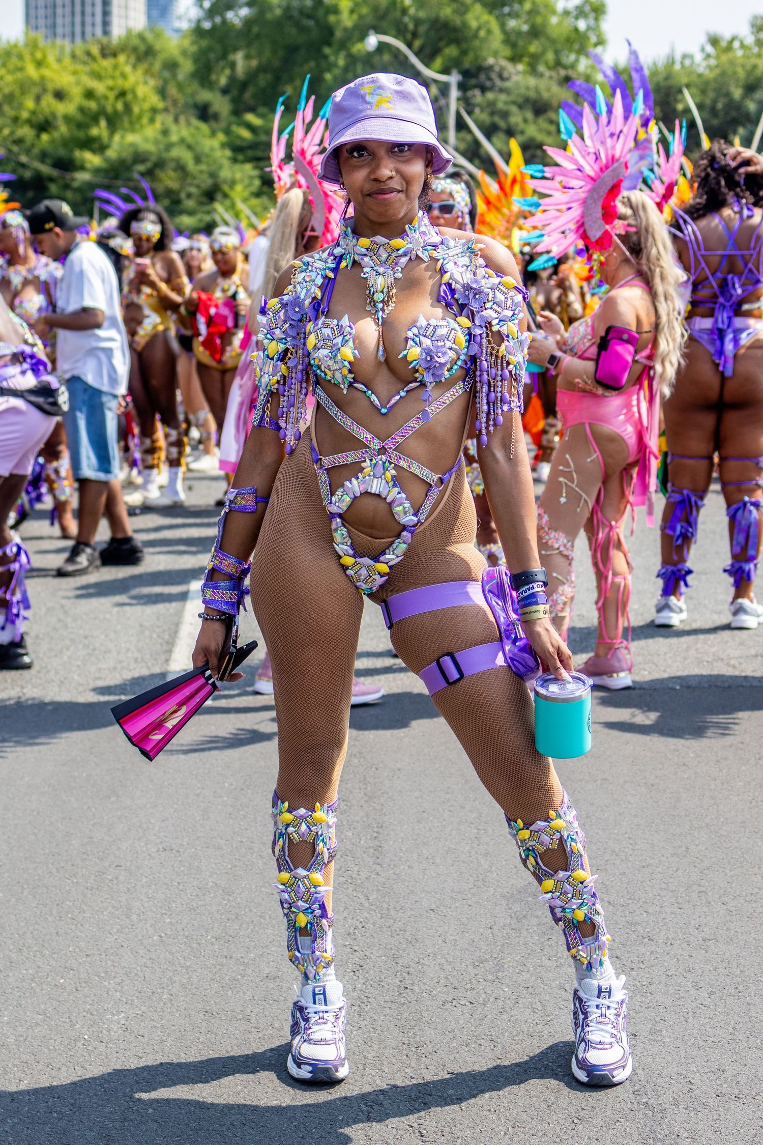 Woman in purple bedazzled carnival costume posing on street during daytime parade celebration.
