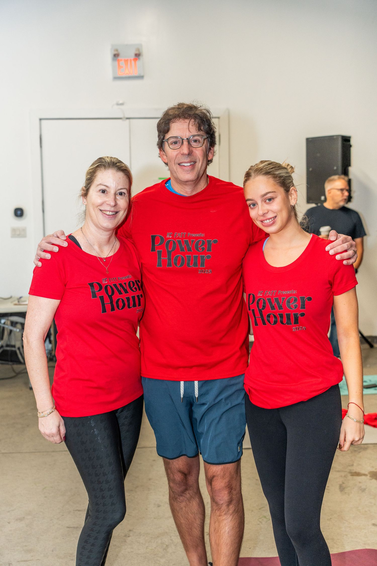 Three people in red Power Hour t-shirts posing together at a fitness event.