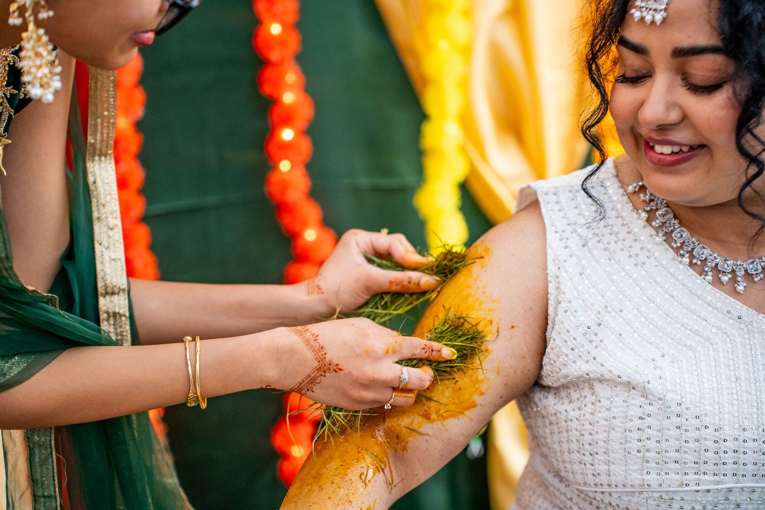 Woman applies turmeric haldi paste to bride's arm during traditional Indian wedding ceremony.