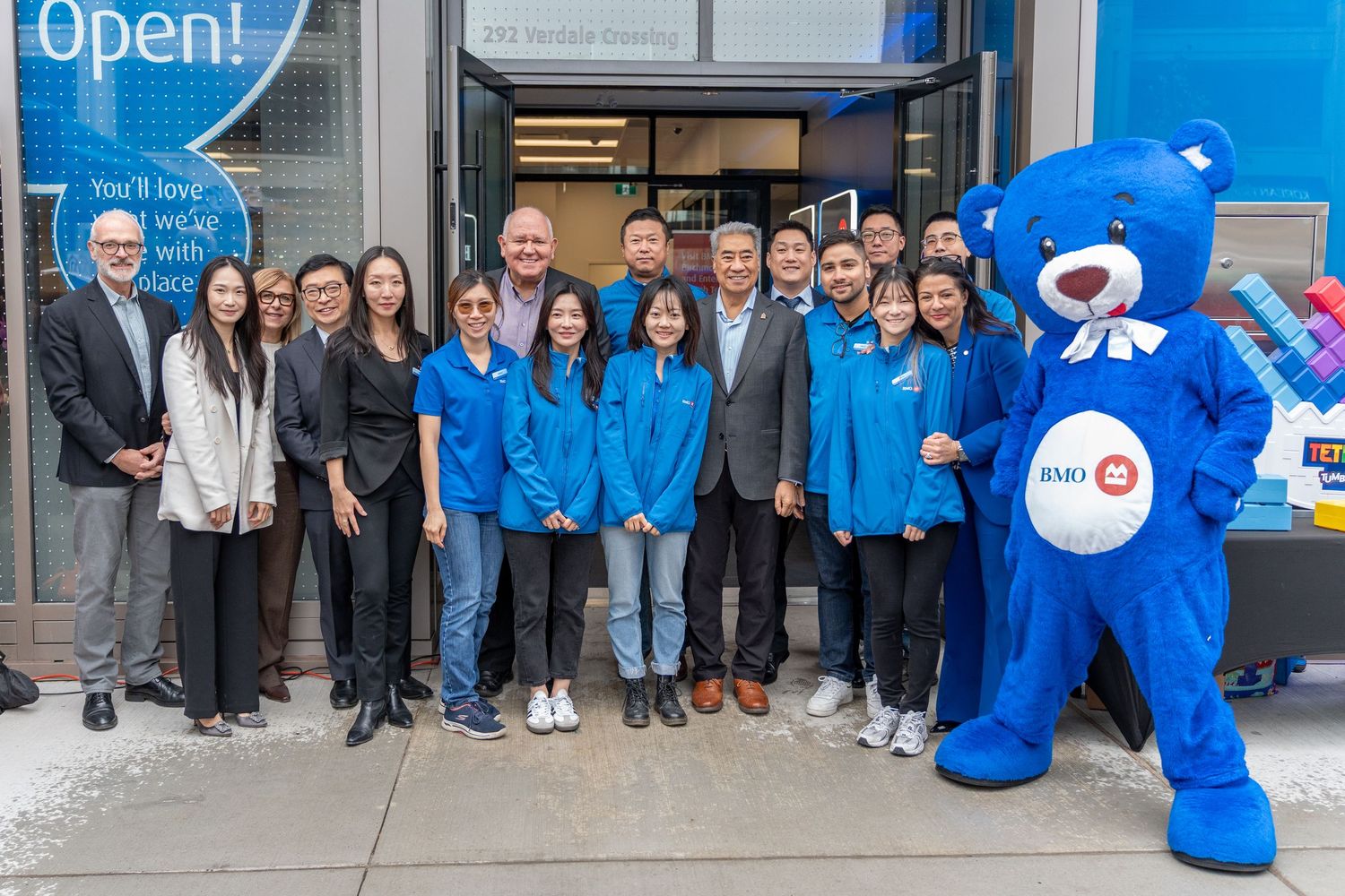 BMO bank staff and team posing with blue bear mascot outside new branch.