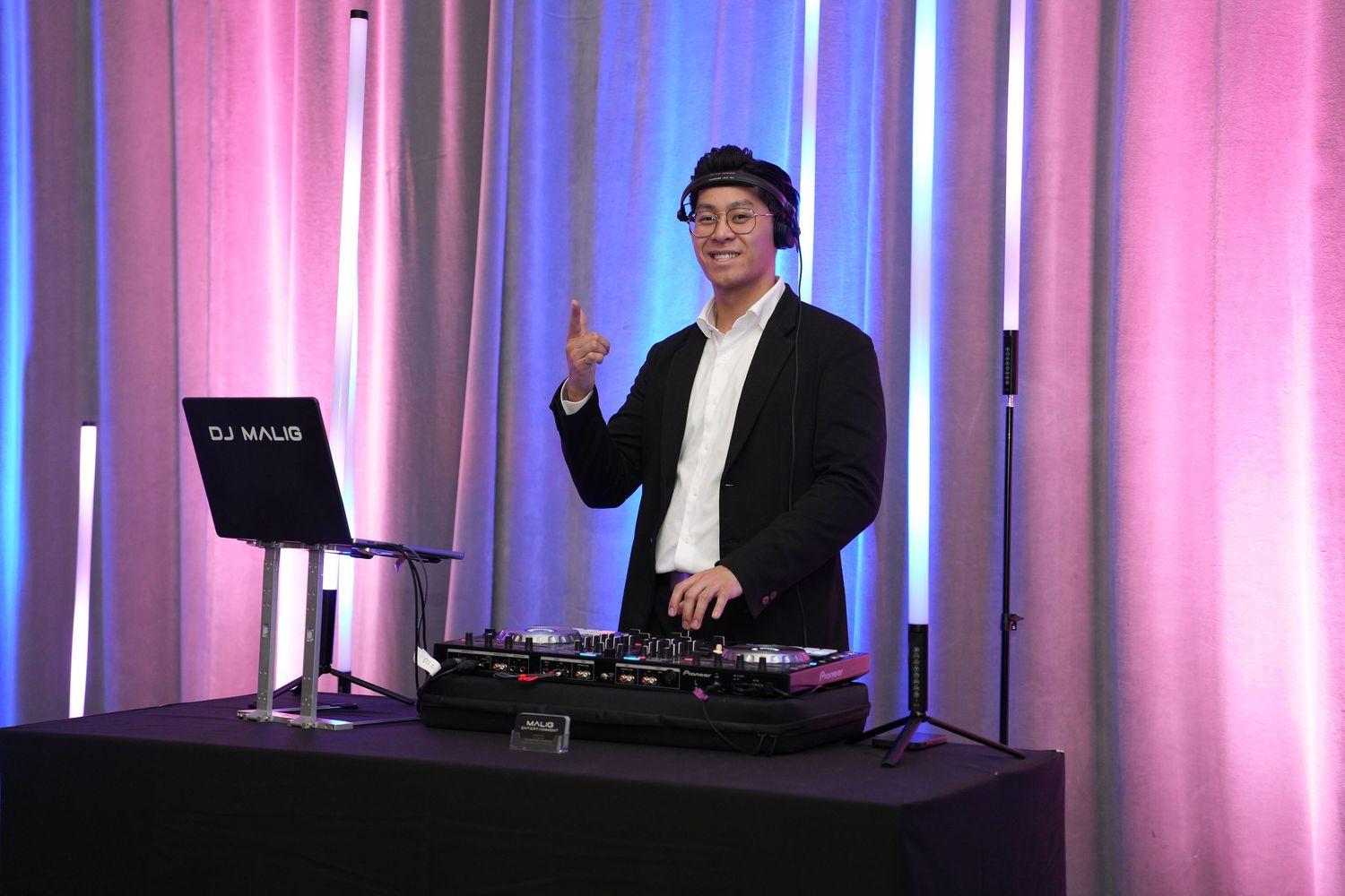 DJ Malis poses at turntables under purple and blue lights at a formal indoor event.