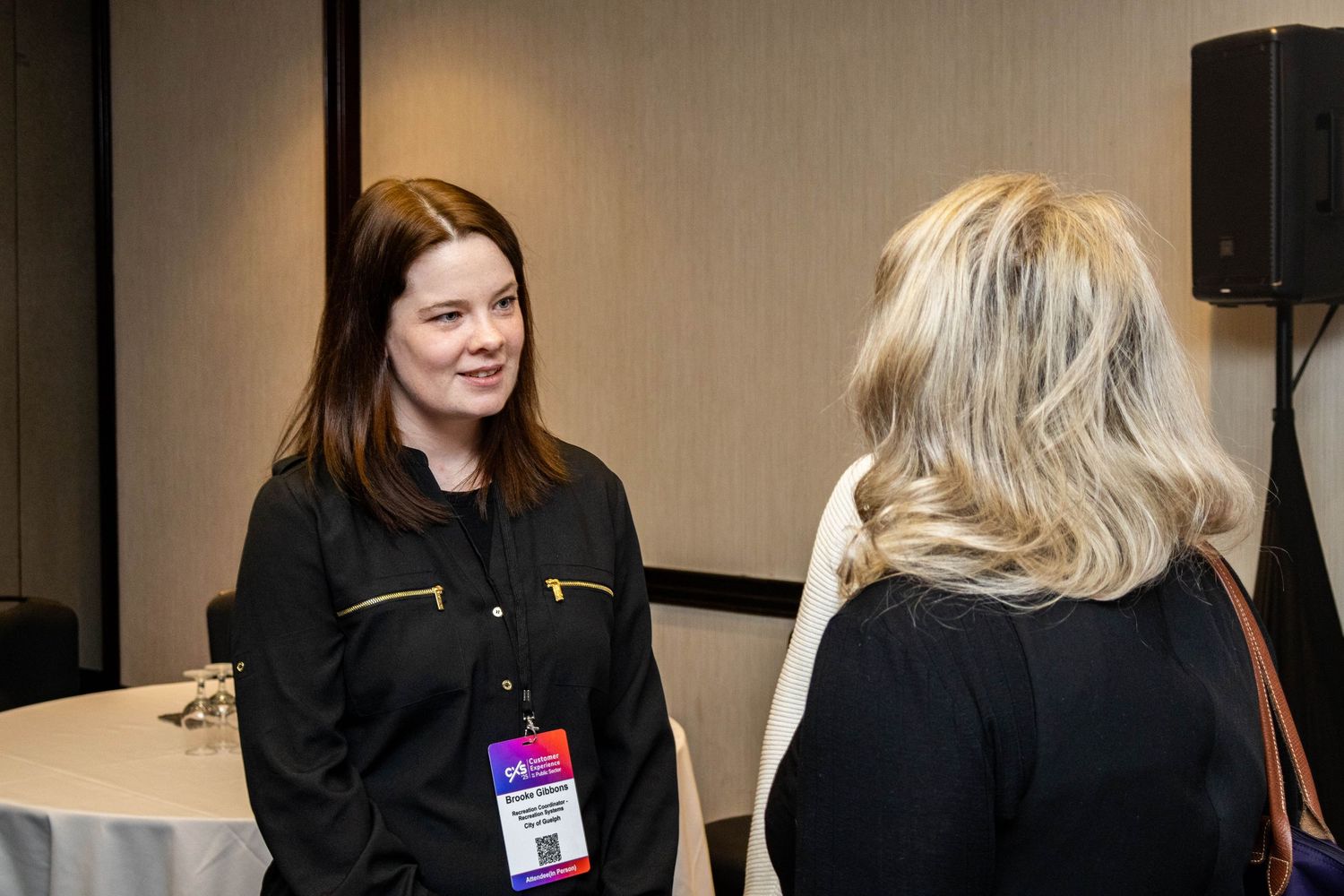 Two professional women networking and conversing at an indoor business conference event.