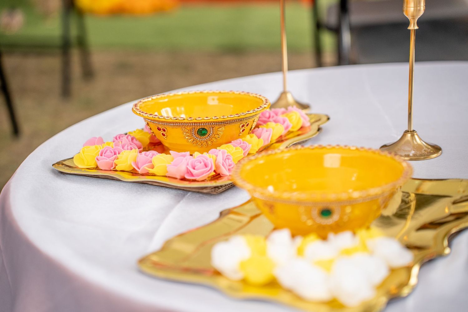 Golden ceremonial bowls with floral decorations on a white table at an Indian Haldi wedding ceremony.