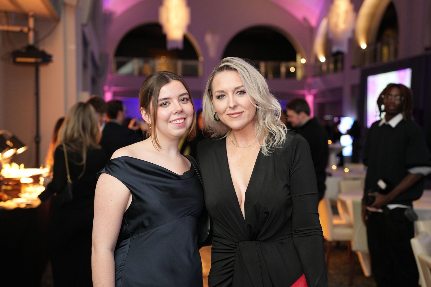 Two women in black formal dresses smiling together at an elegant evening gala event.