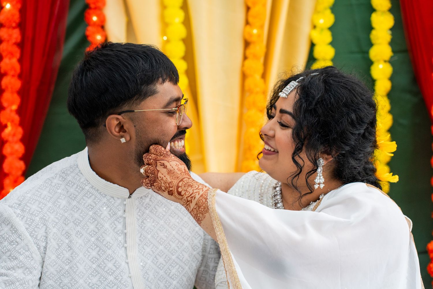 Couple shares a tender moment during Indian wedding ceremony with colorful floral backdrop.