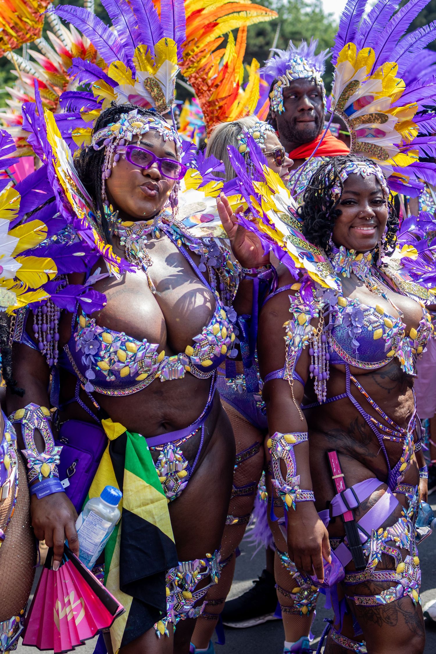 Women in elaborate purple feathered carnival costumes smiling during a vibrant street parade festival.
