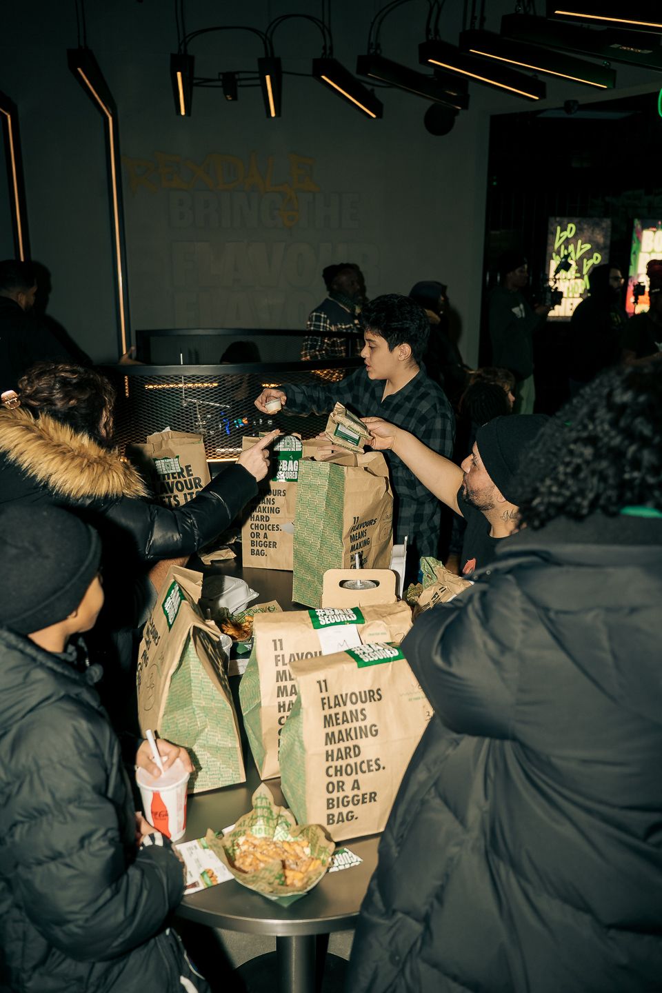 Group of people collecting takeout bags at a busy Wings restaurant counter.