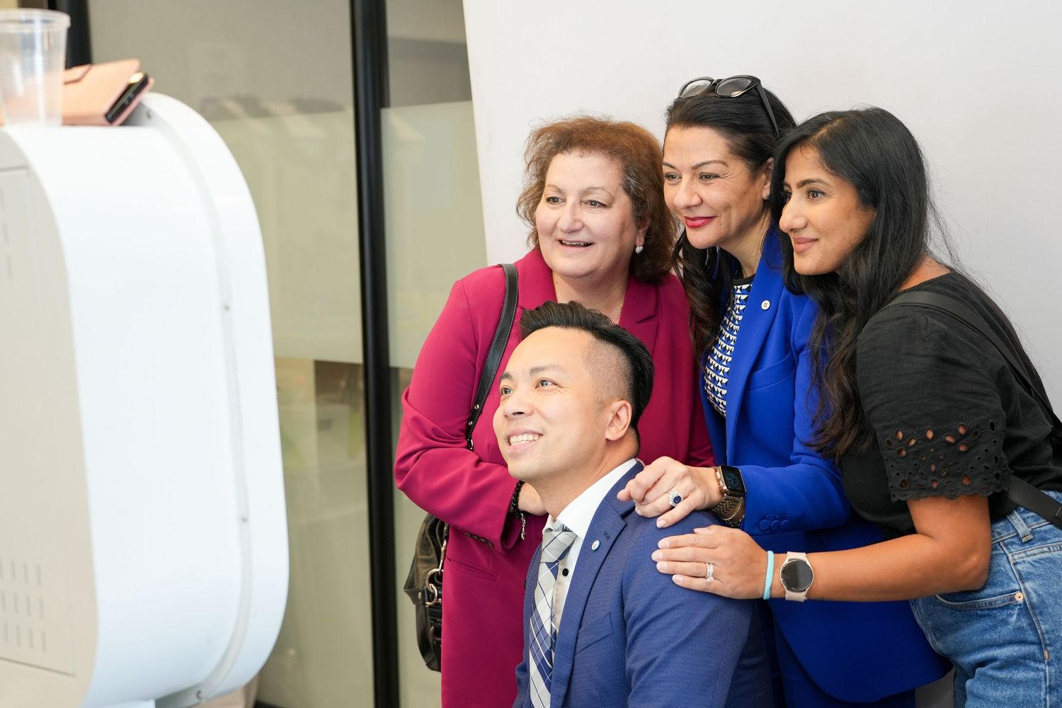 Four diverse colleagues smile together while taking a photo at a modern office event.