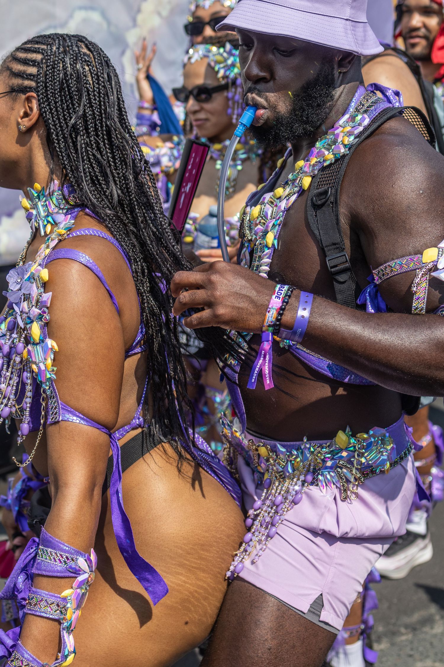 Carnival participants in matching purple beaded costumes celebrating at a street parade festival.