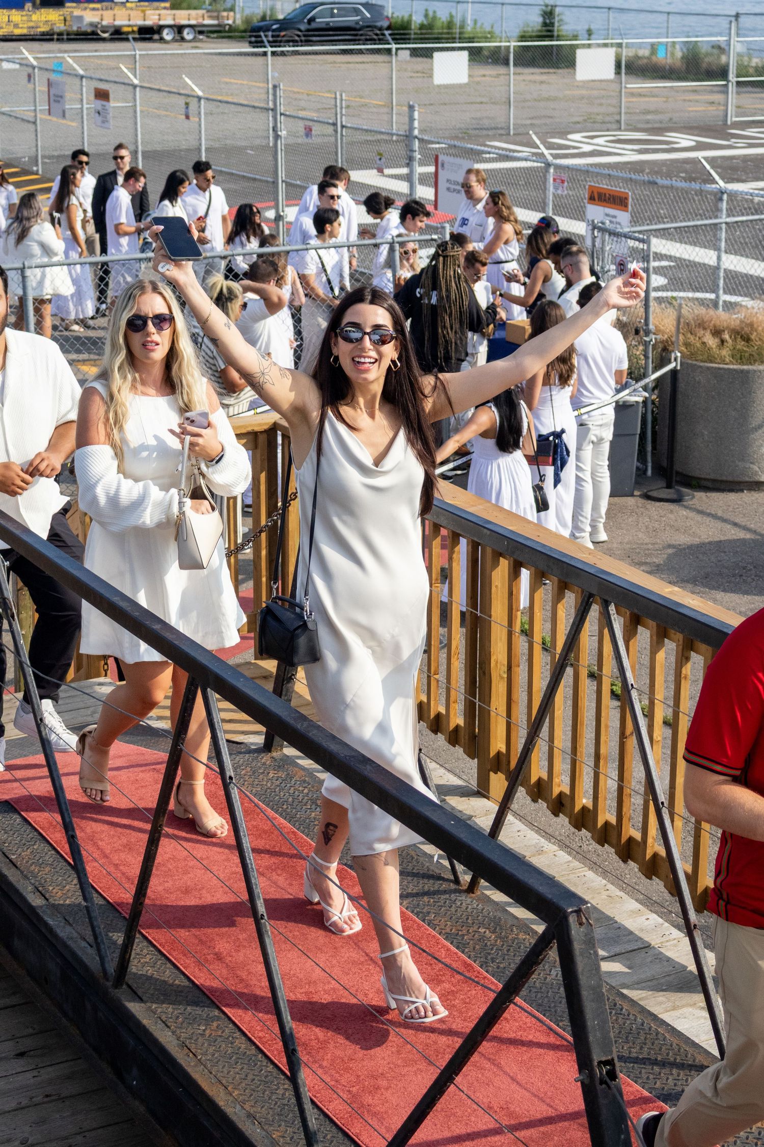 Woman in white dress with arms raised walking up red carpet stairs at party.