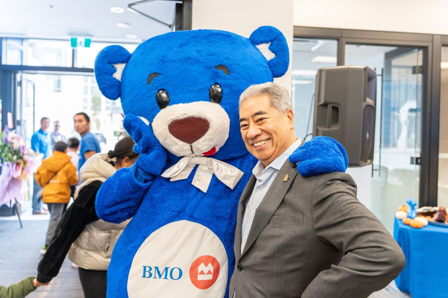Man in suit poses with BMO blue bear mascot at a bank event.
