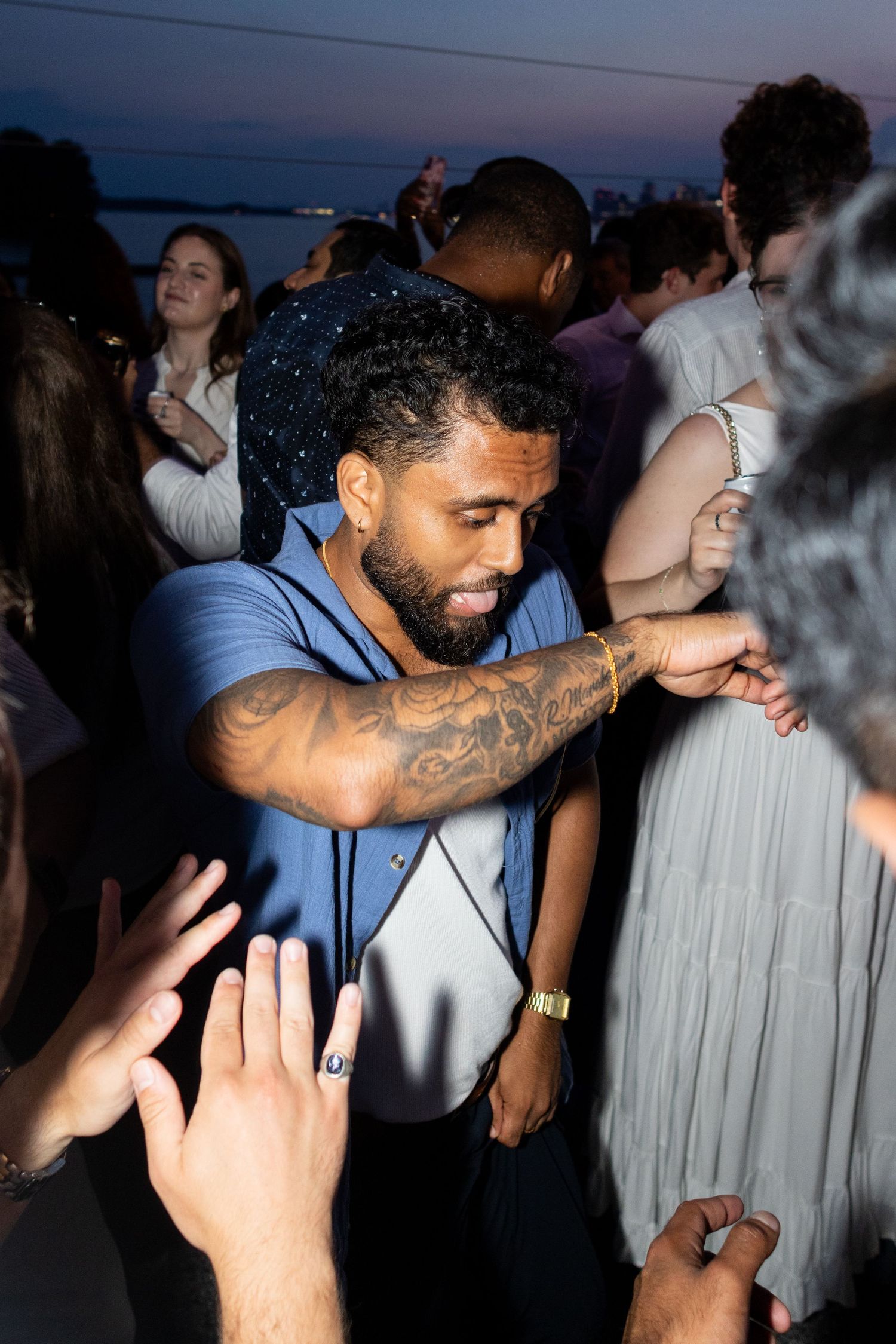 Man with tattoos dancing at an outdoor evening party near the waterfront.