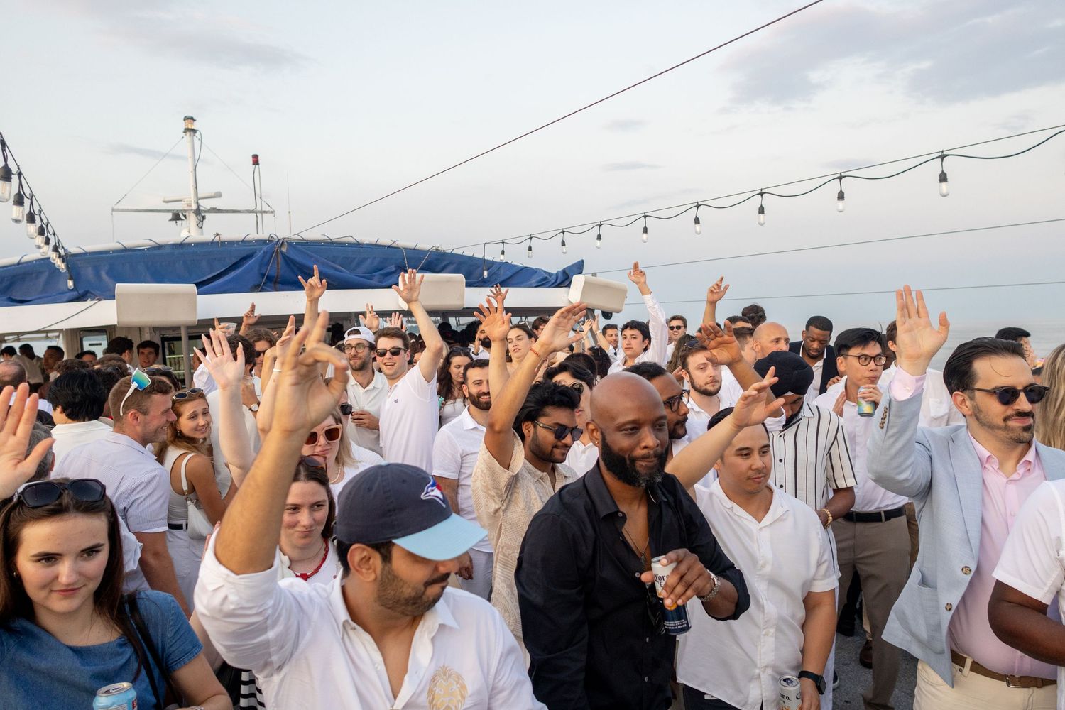 Crowd of people in white outfits dancing at an outdoor rooftop party at sunset.