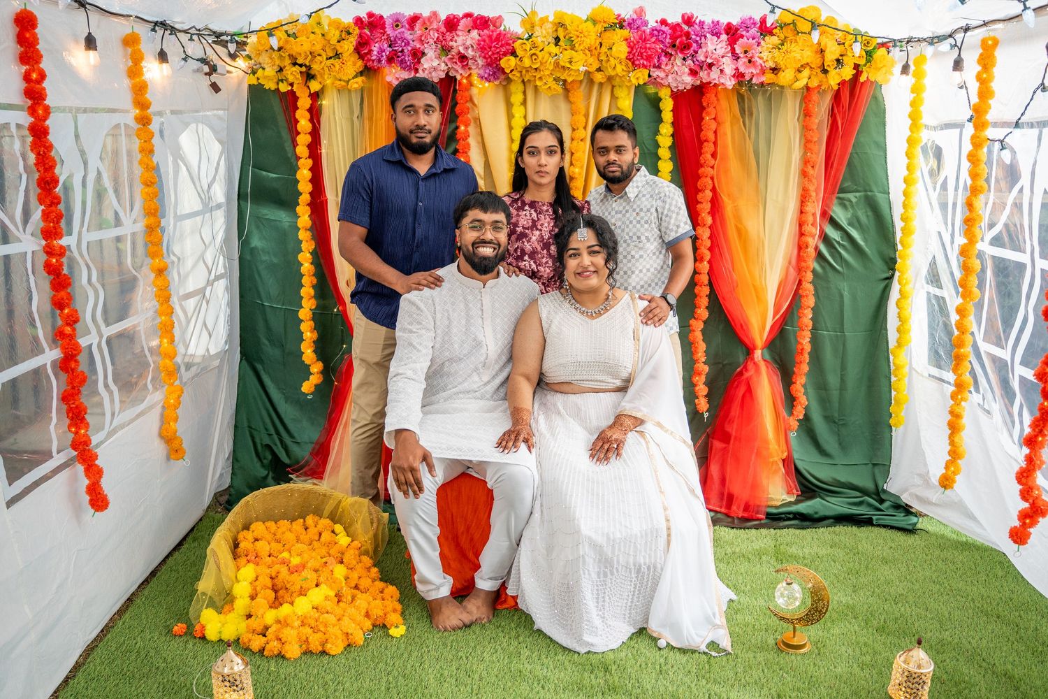 Family of five poses together under vibrant floral decorations at an Indian celebration event.