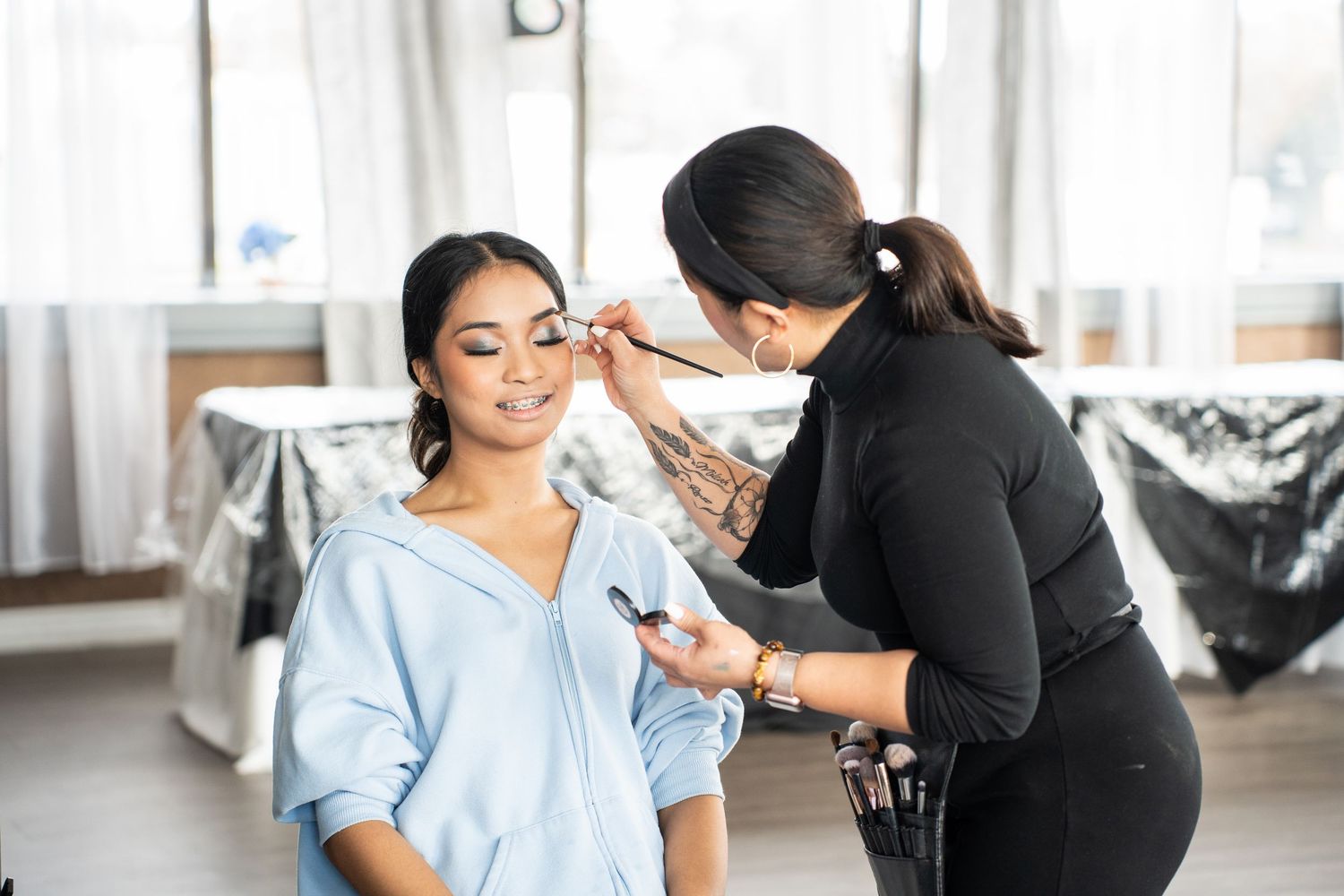 Young woman smiling as makeup artist applies professional makeup for her 18th birthday debut celebration.