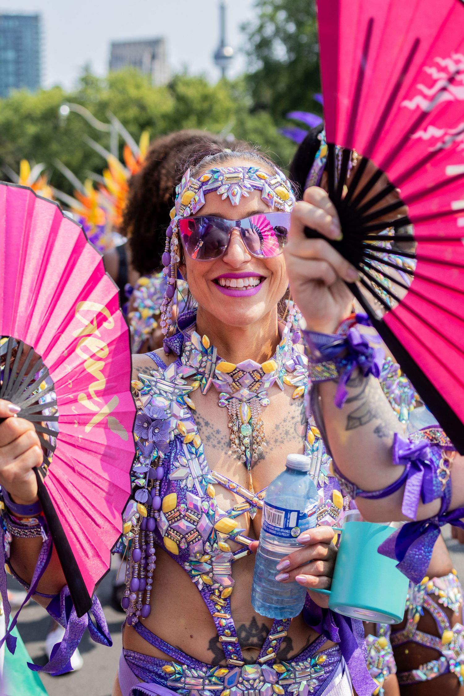 Vibrant carnival performer in purple beaded costume holding colorful fans at summer street parade festival.