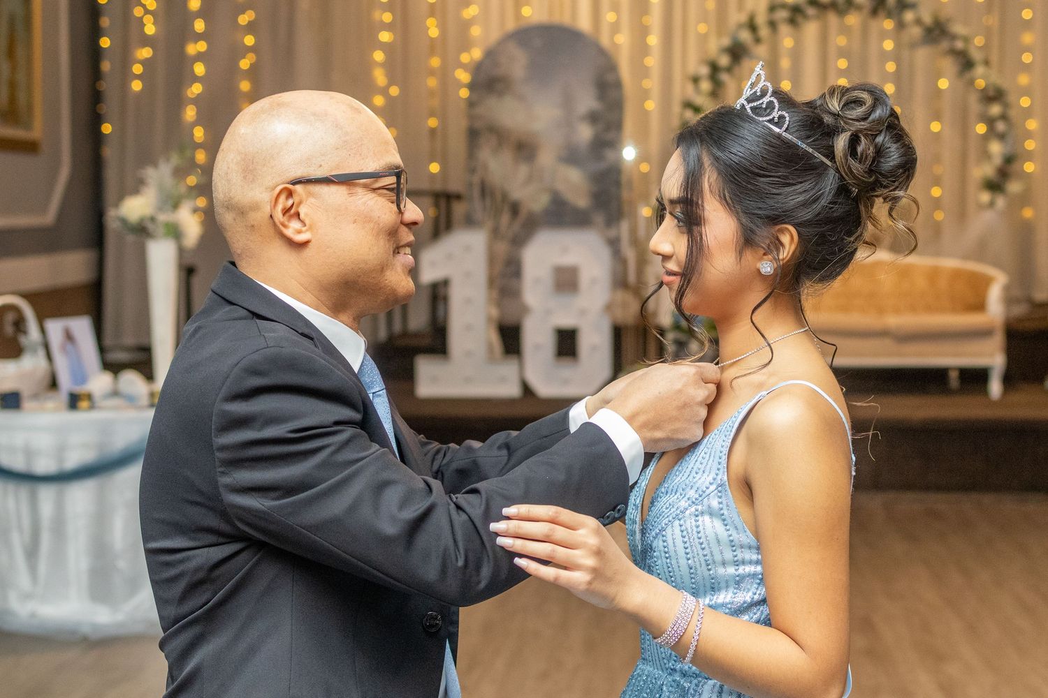 Father adjusting daughter's necklace during an emotional moment at her 18th birthday debut celebration.