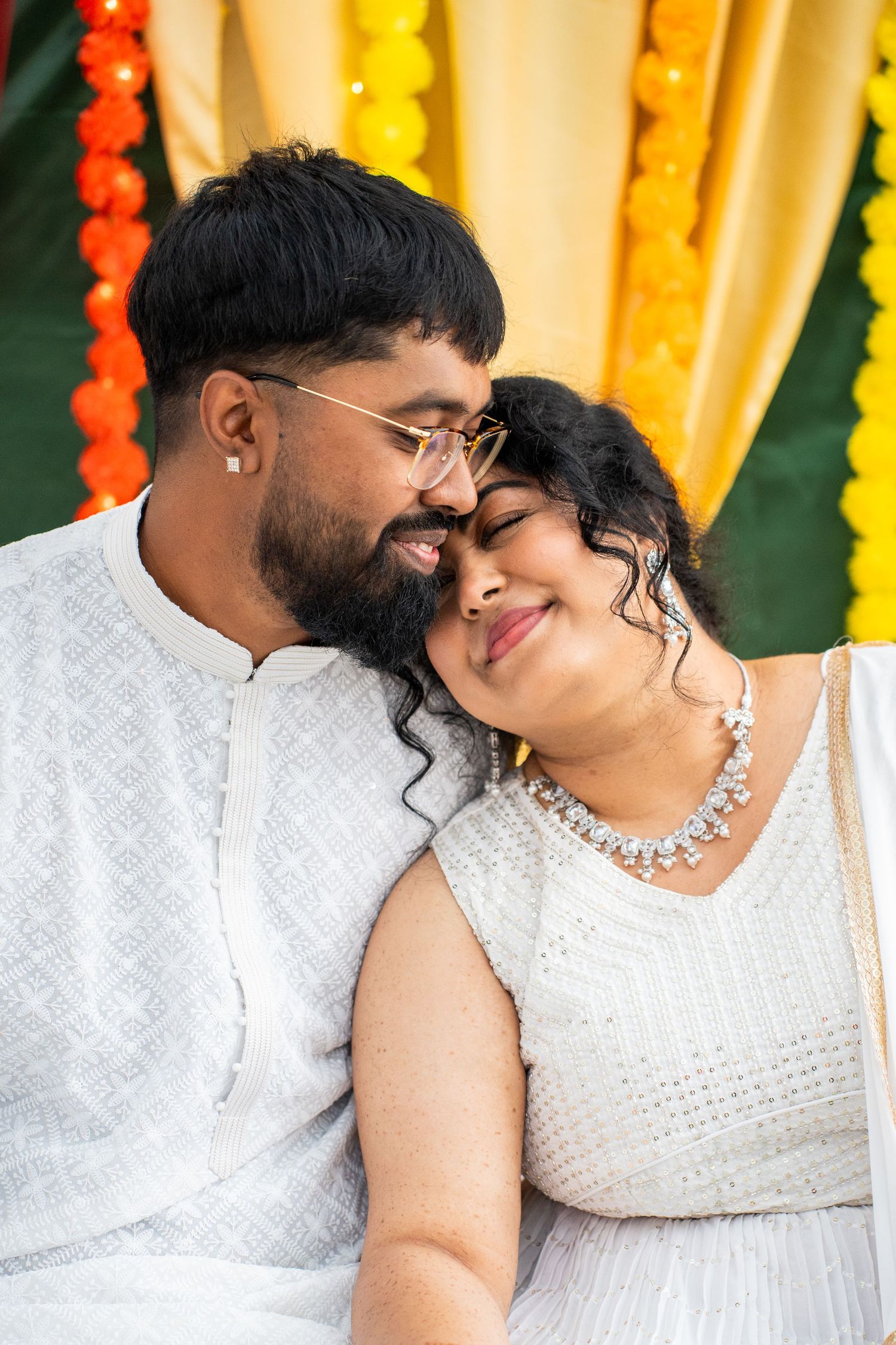Couple in white traditional Indian attire share a romantic close moment at festive celebration.
