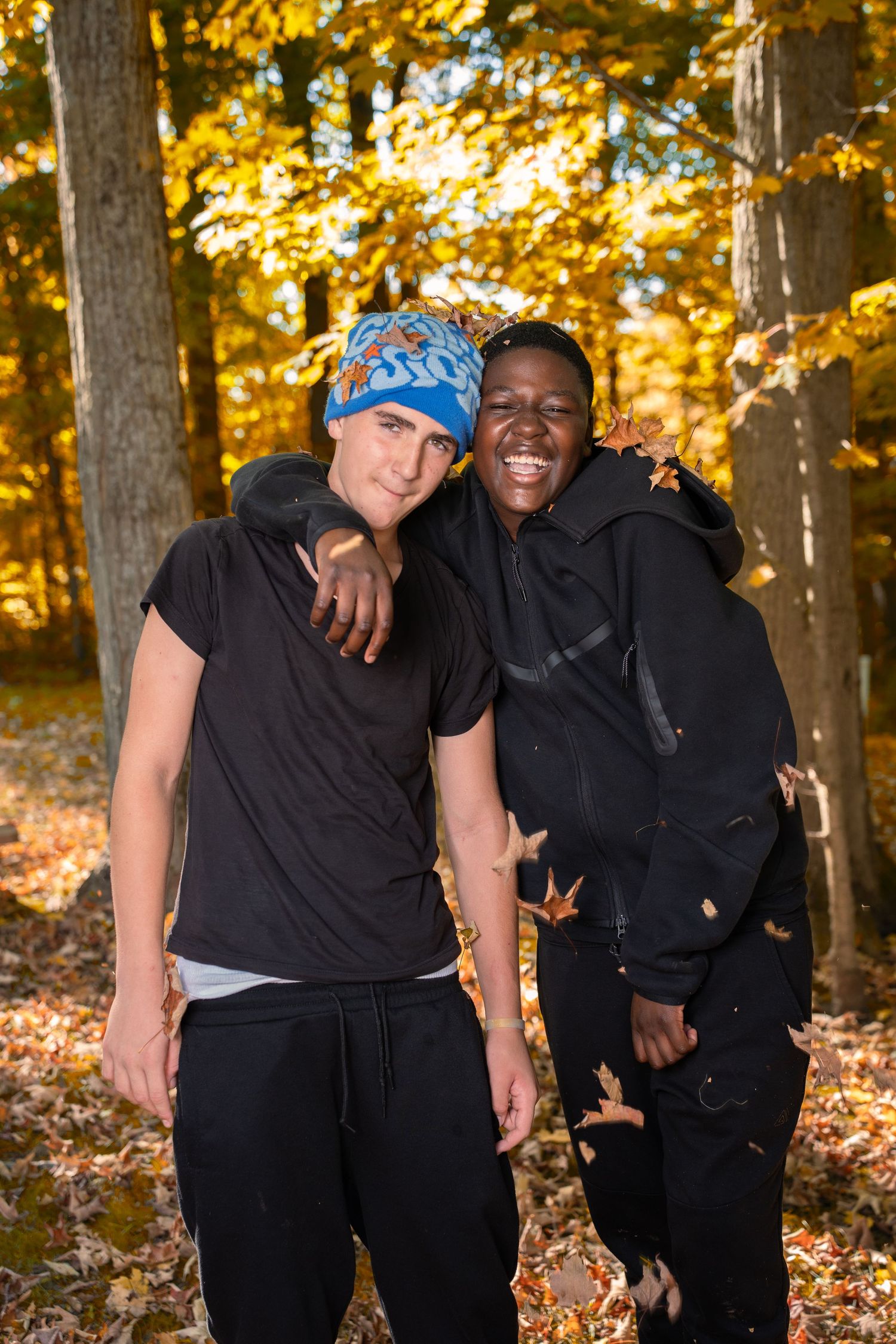 Two friends smiling and embracing in a sunlit autumn forest with golden foliage.