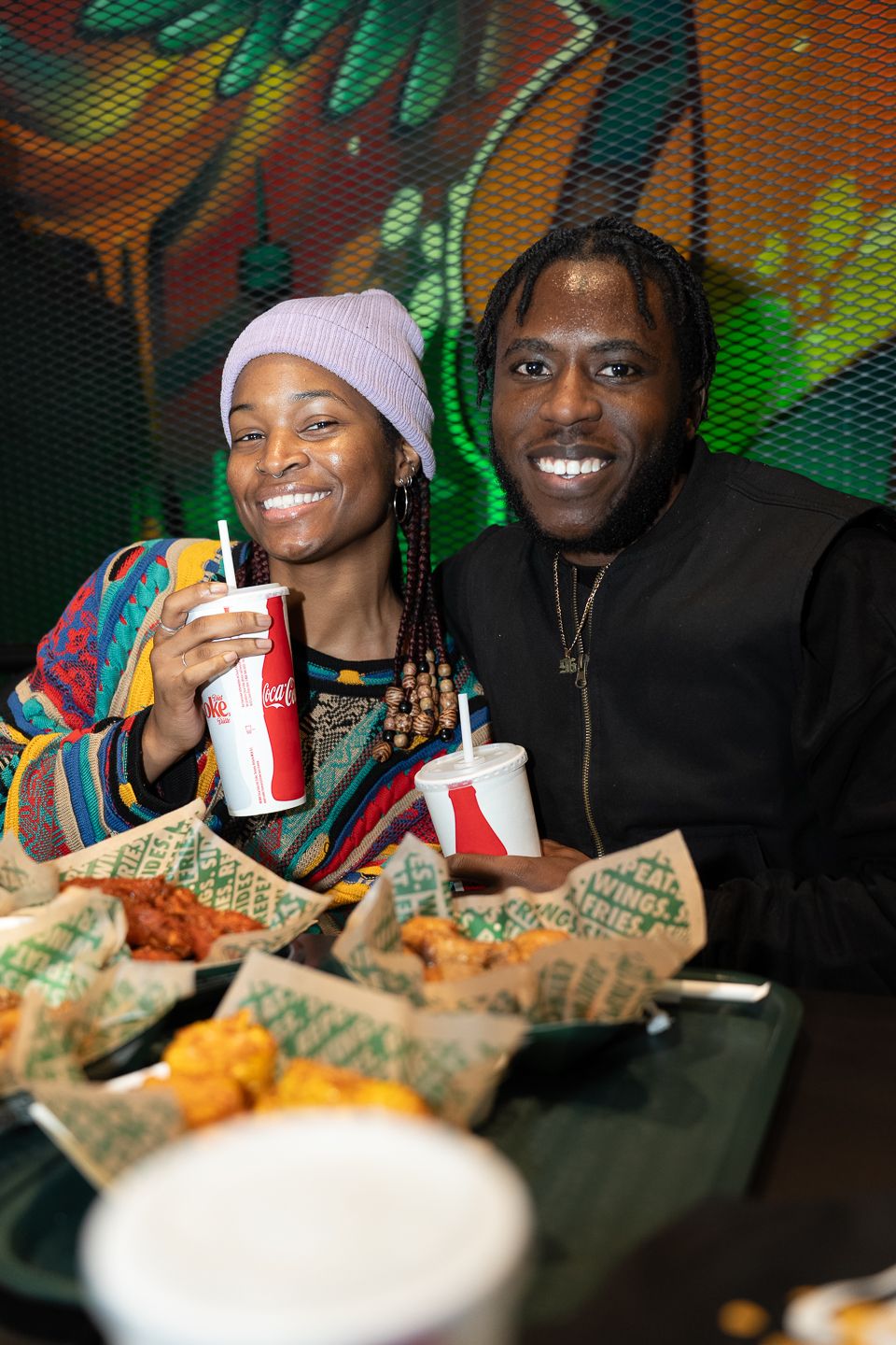 Couple smiling and holding Coca-Cola drinks at a Wings restaurant with food on the table.