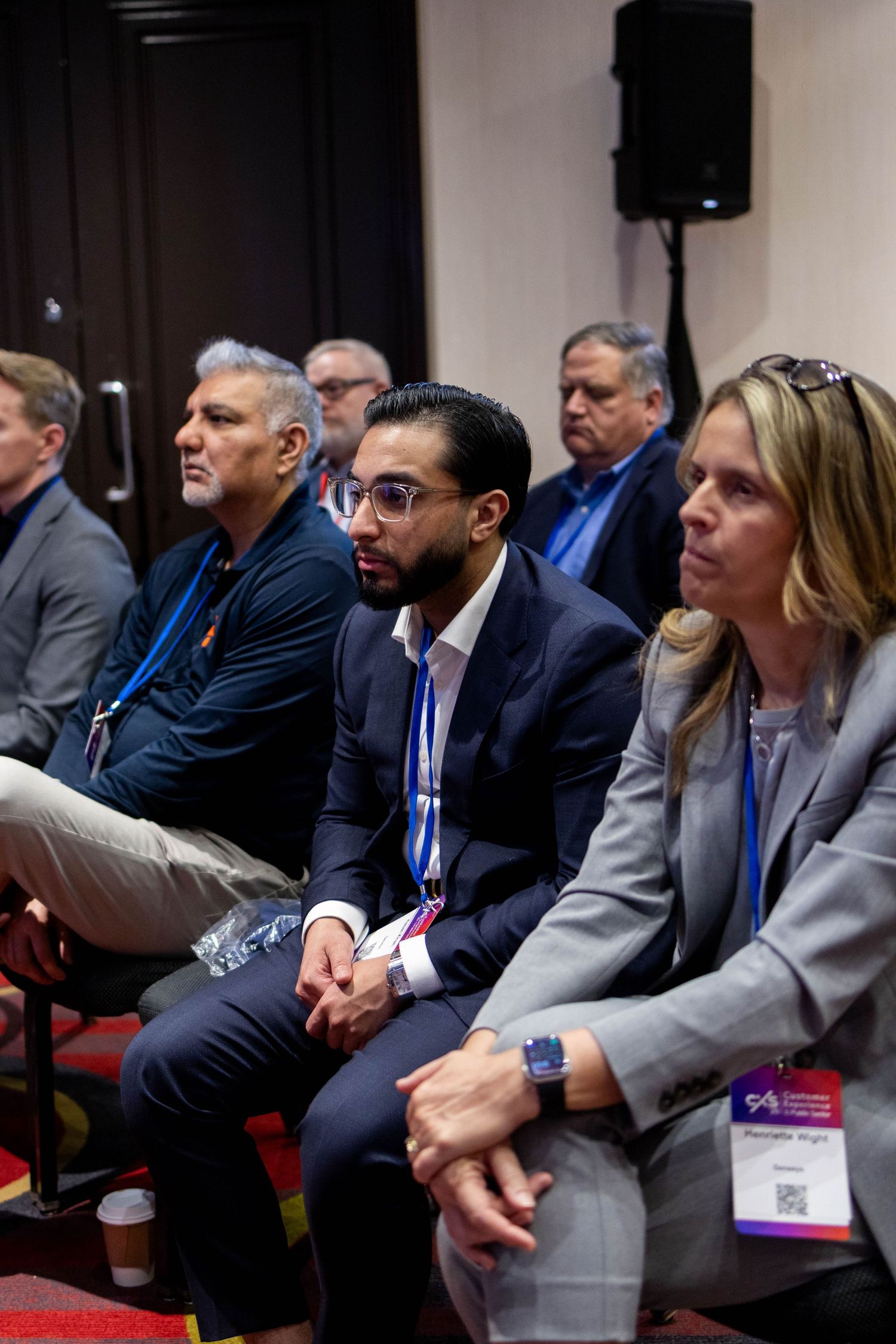 Professionals in business attire seated at a conference, attentively listening to a presentation.