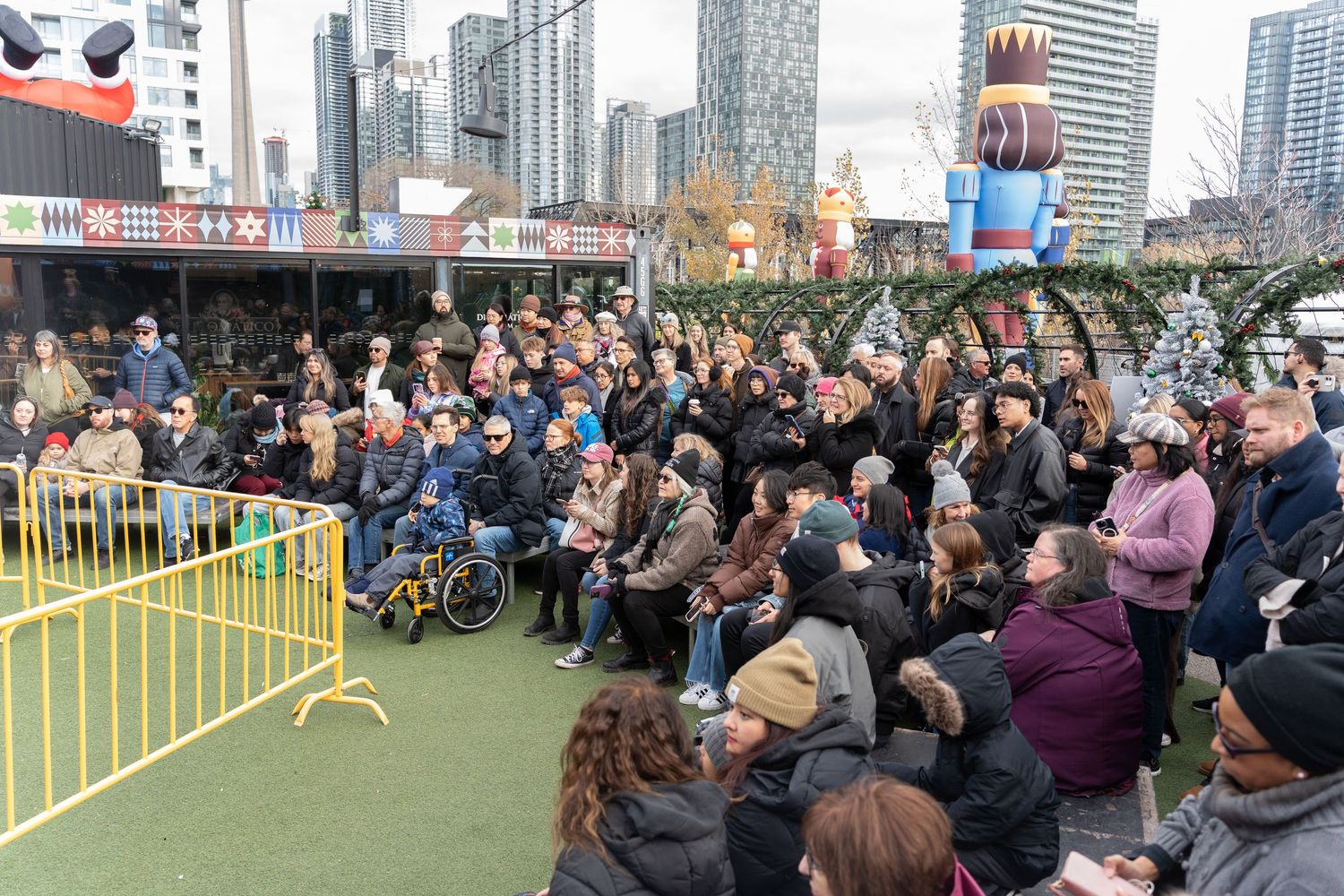 Large crowd of people gathered outdoors watching a performance at a festive winter market event.