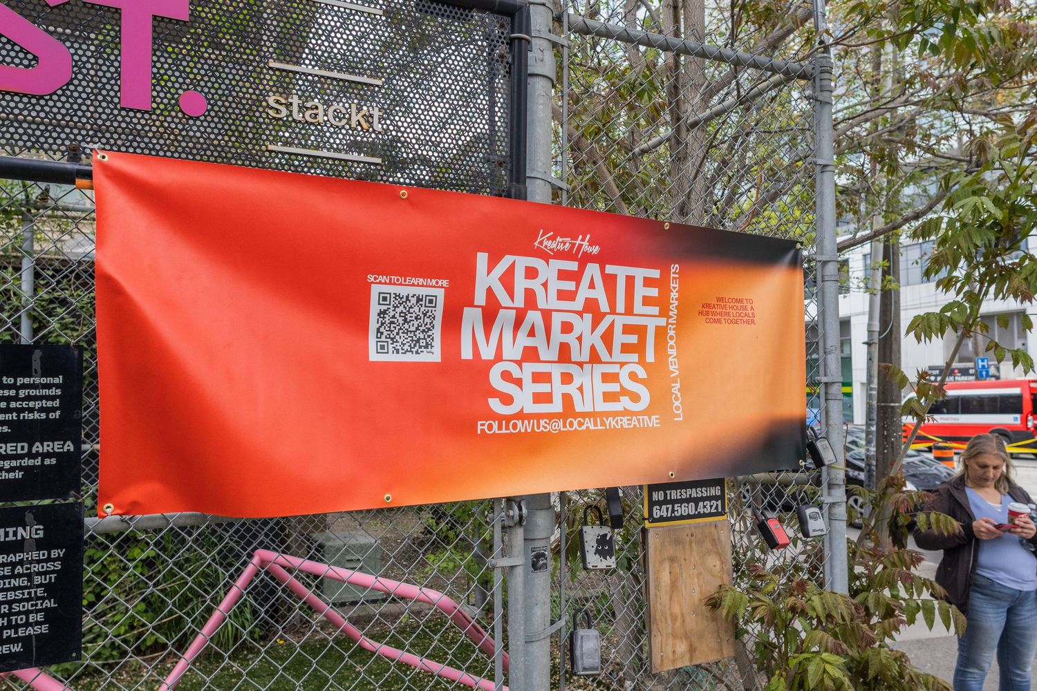 Orange Kreate Market Series banner with QR code displayed on a chain-link fence at an outdoor market.